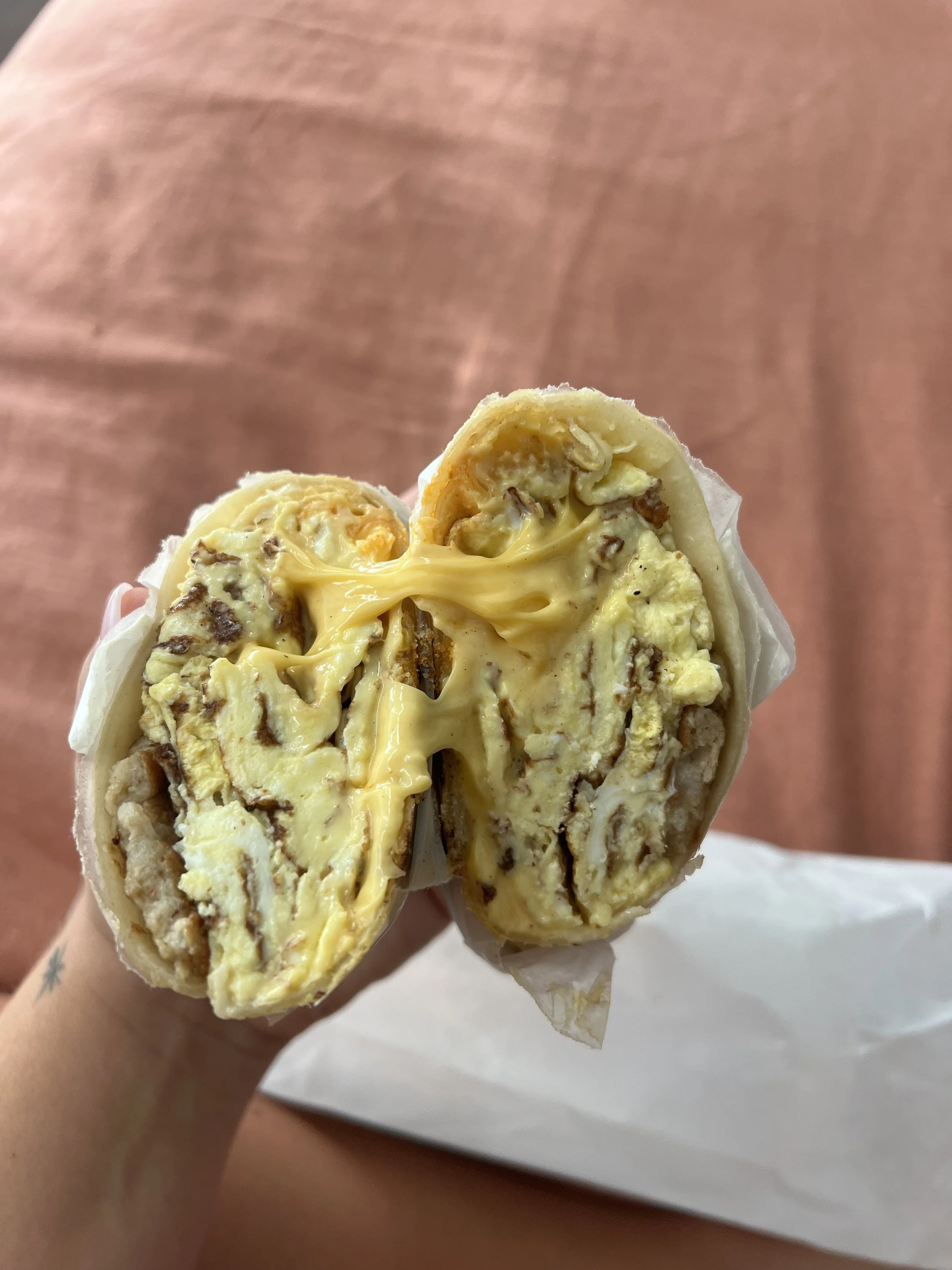 Close-up of a breakfast burrito with scrambled eggs, cheese, and sausage inside a tortilla.