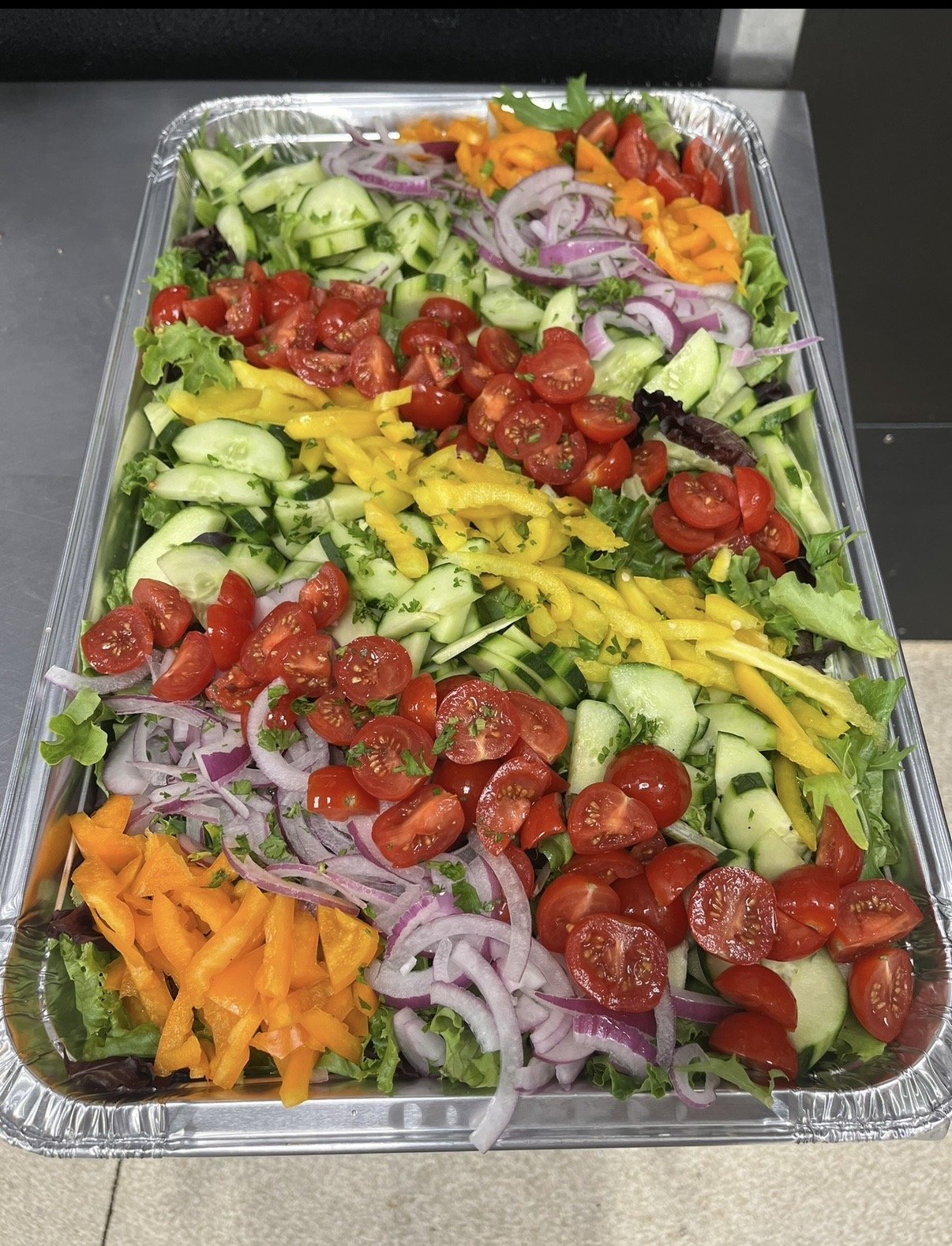 Tray of chopped fresh vegetables including cherry tomatoes, cucumbers, red onions, bell peppers, and mixed greens.