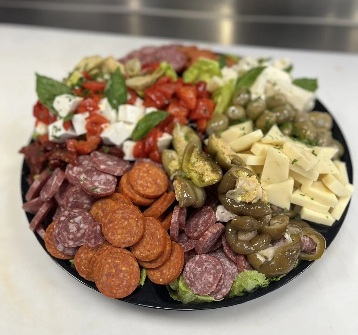 A black circular platter with an assortment of cured meats, cheeses, olives, and vegetables arranged in sections.