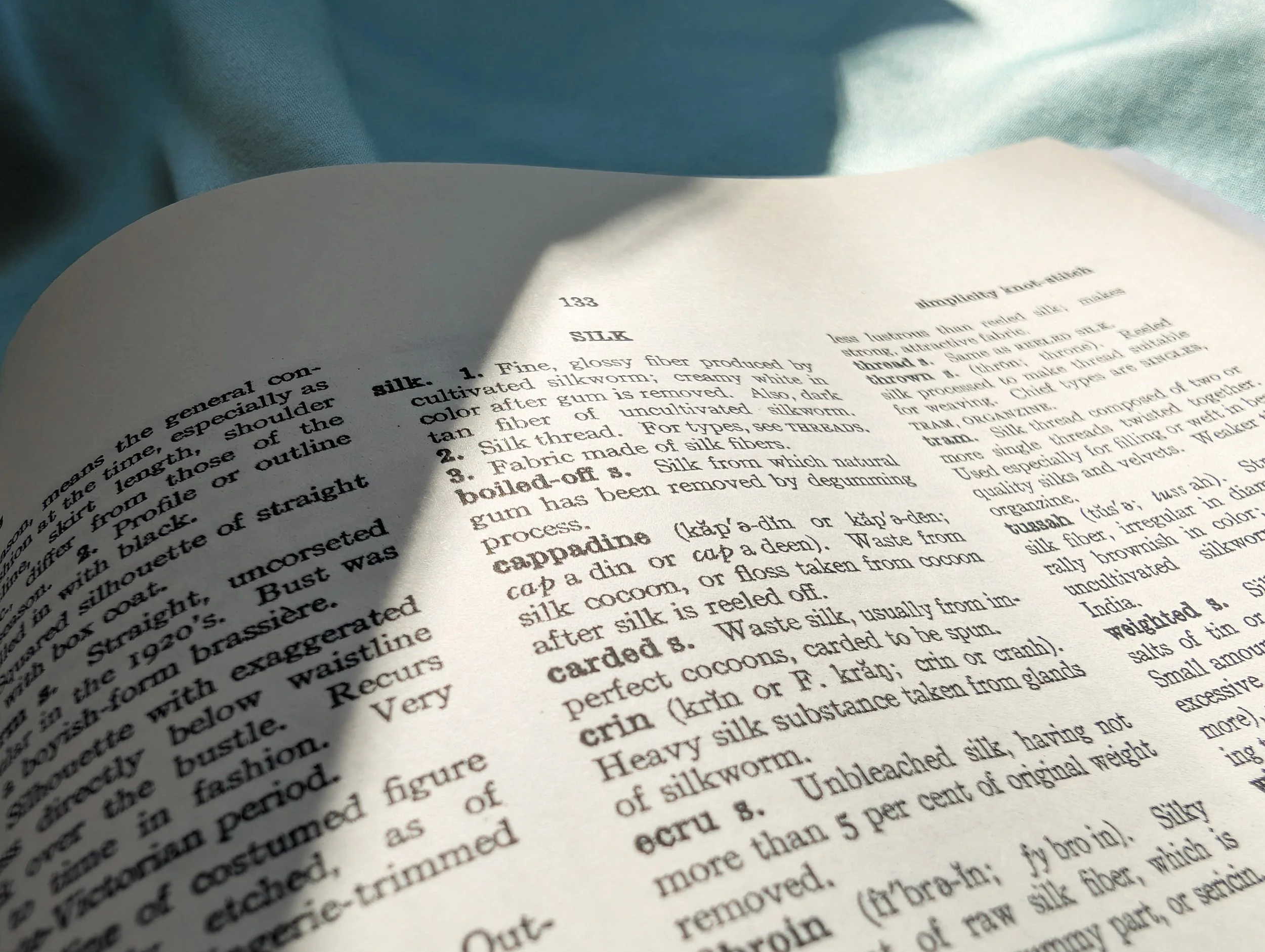 A sewing needle piercing through beige fabric with white thread.