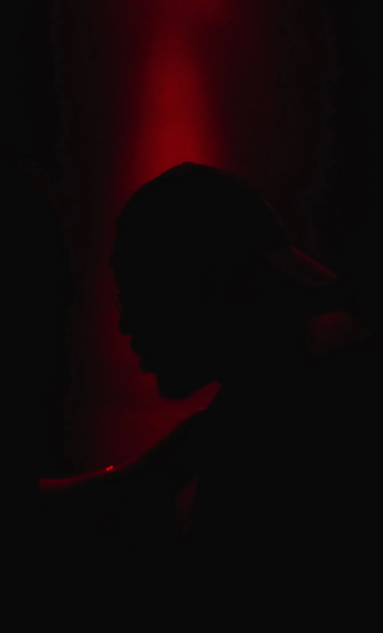 Silhouette of a person wearing a cap against a red light background.