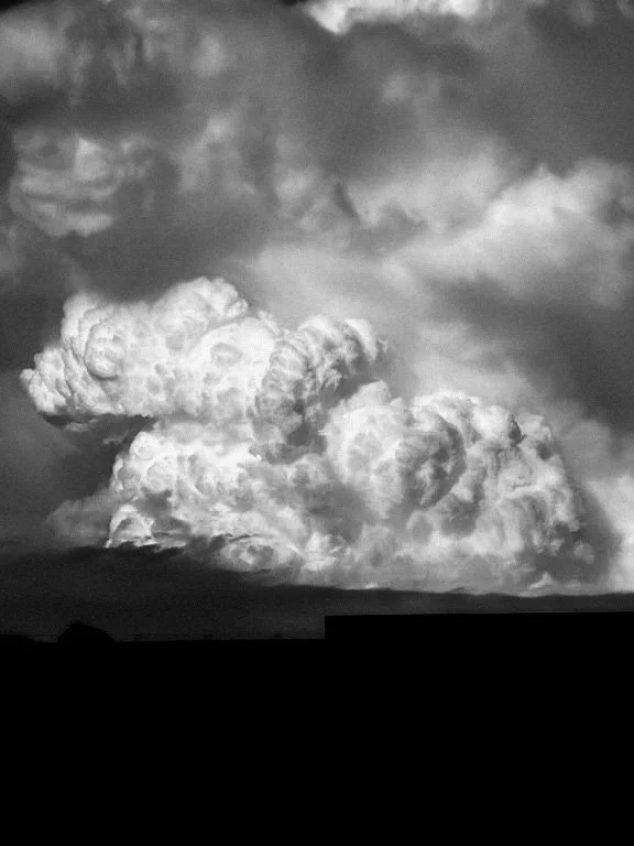 Black and white photo of large, billowing cloud formation in the sky above a flat landscape.