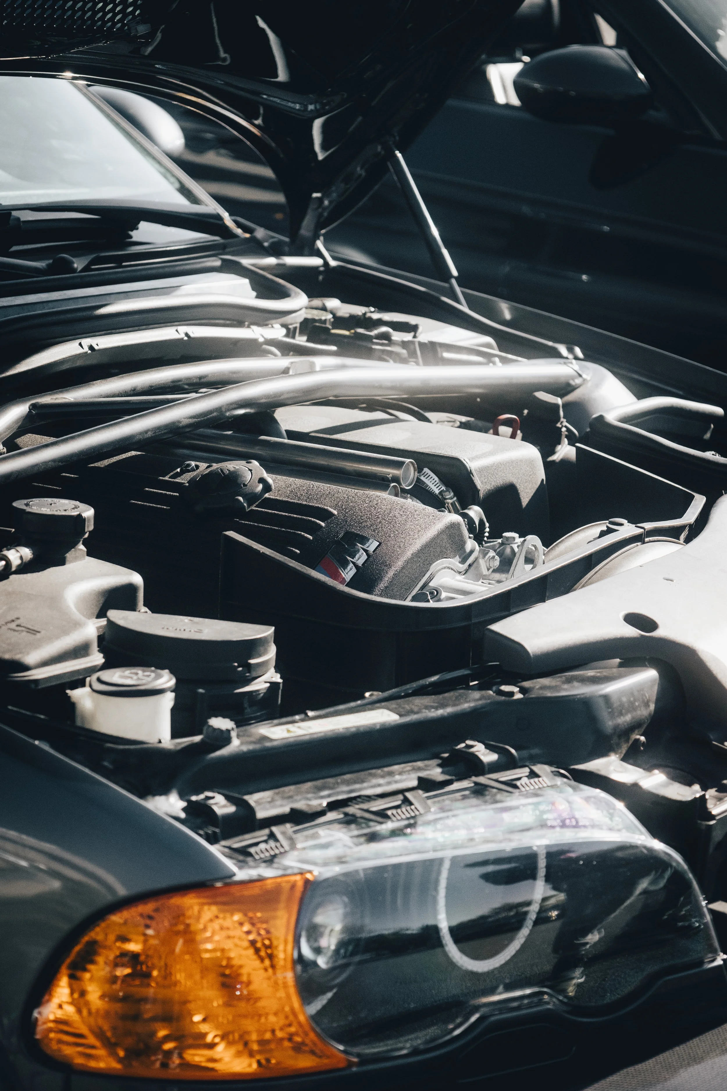 Open car hood revealing engine with various mechanical parts and components in a black vehicle.