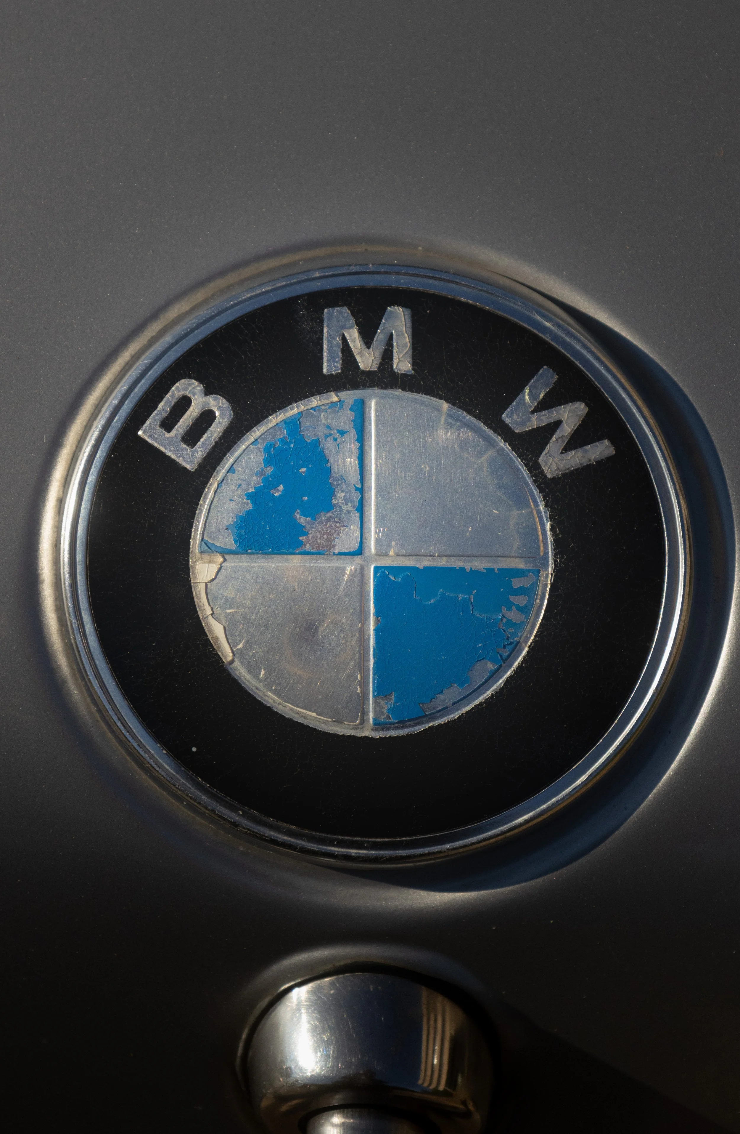 Close-up of a BMW emblem with peeling blue and white paint on a gray background.