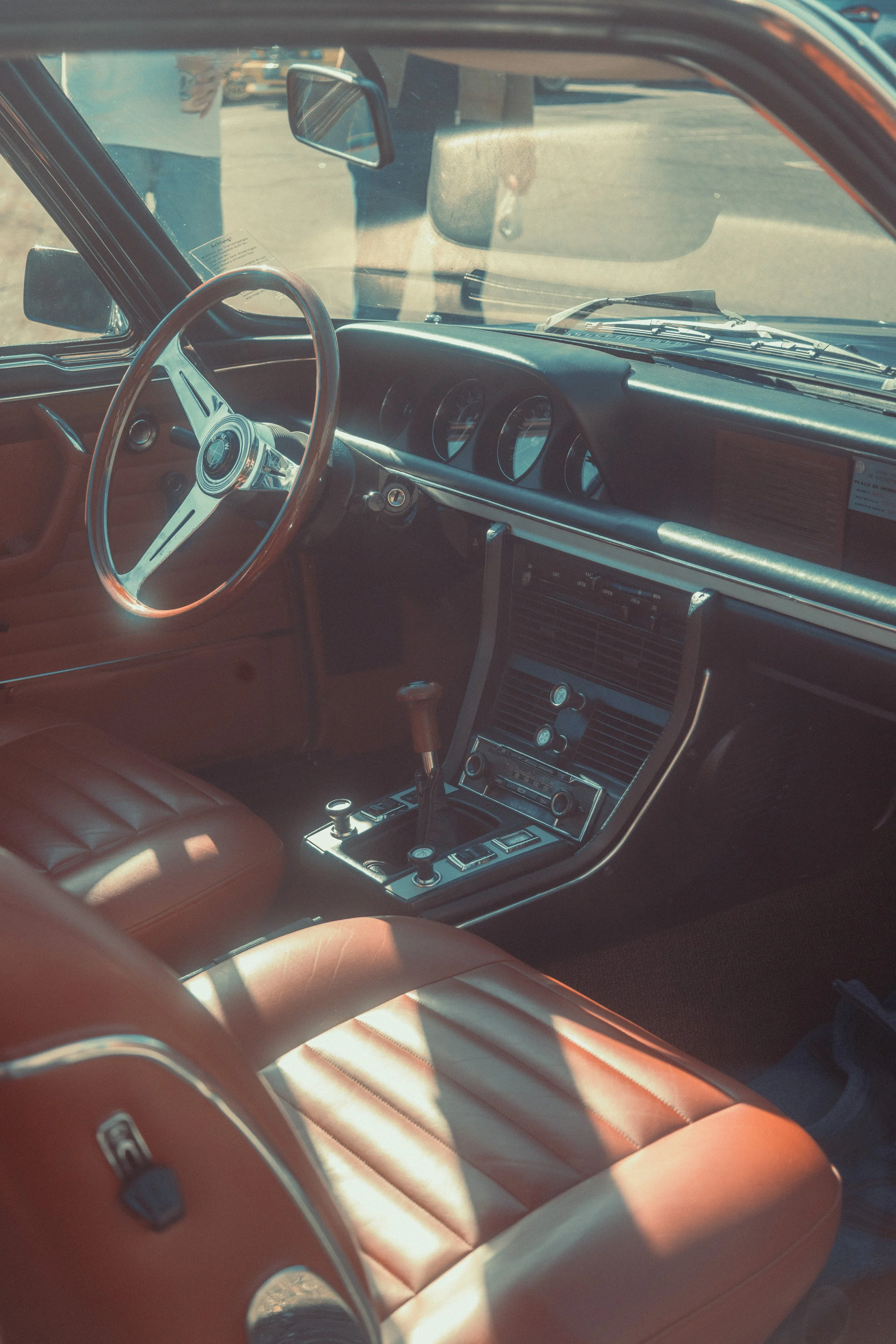 Interior view of a vintage car with tan leather seats, a wood-rimmed steering wheel, and a dashboard with multiple gauges and control knobs.