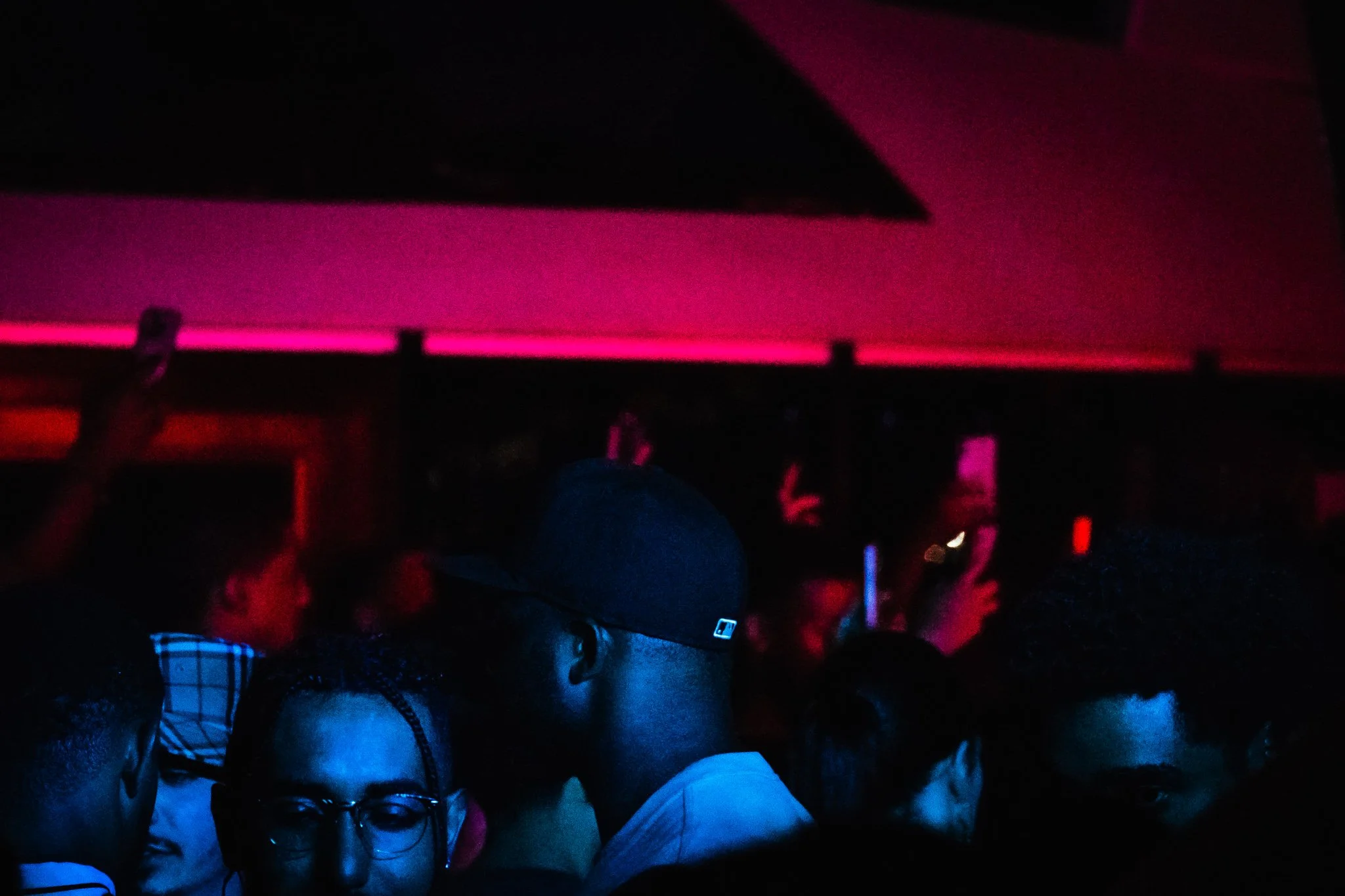 Crowd of people at a dimly lit event with pink and red lighting.
