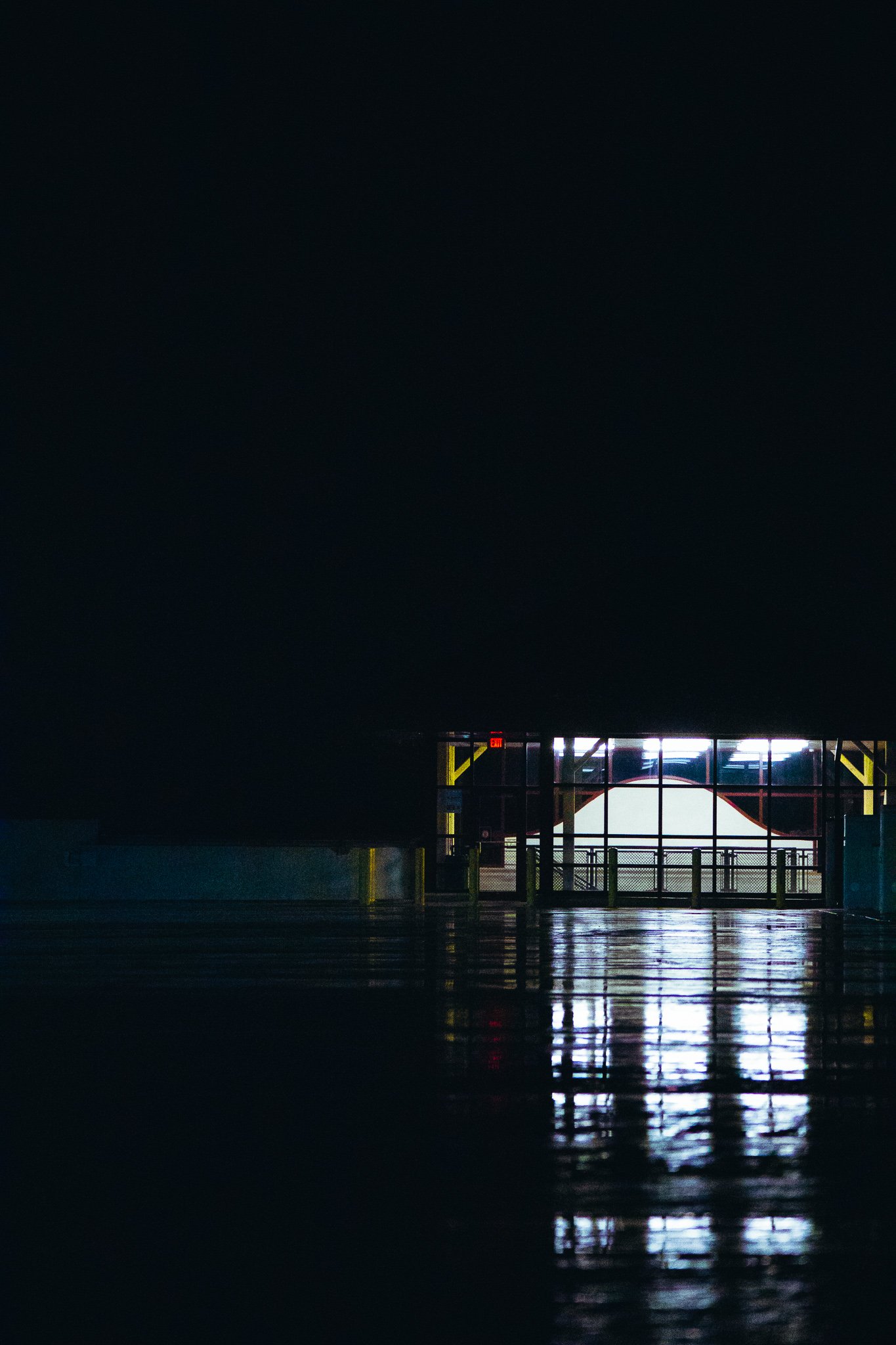 Brightly lit exit door at the end of a dark, reflective parking garage.