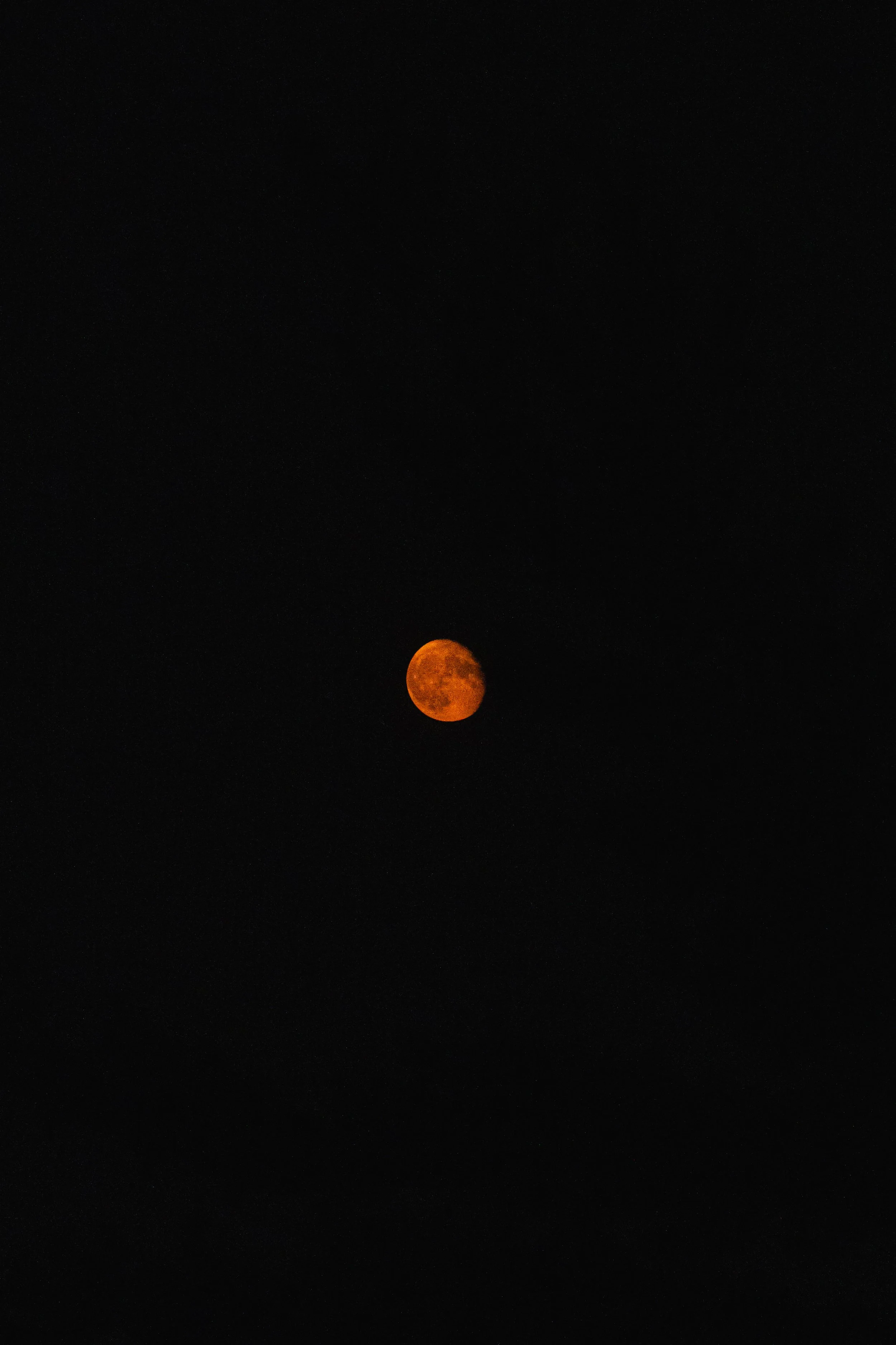 The image shows a reddish-orange moon against a dark night sky.