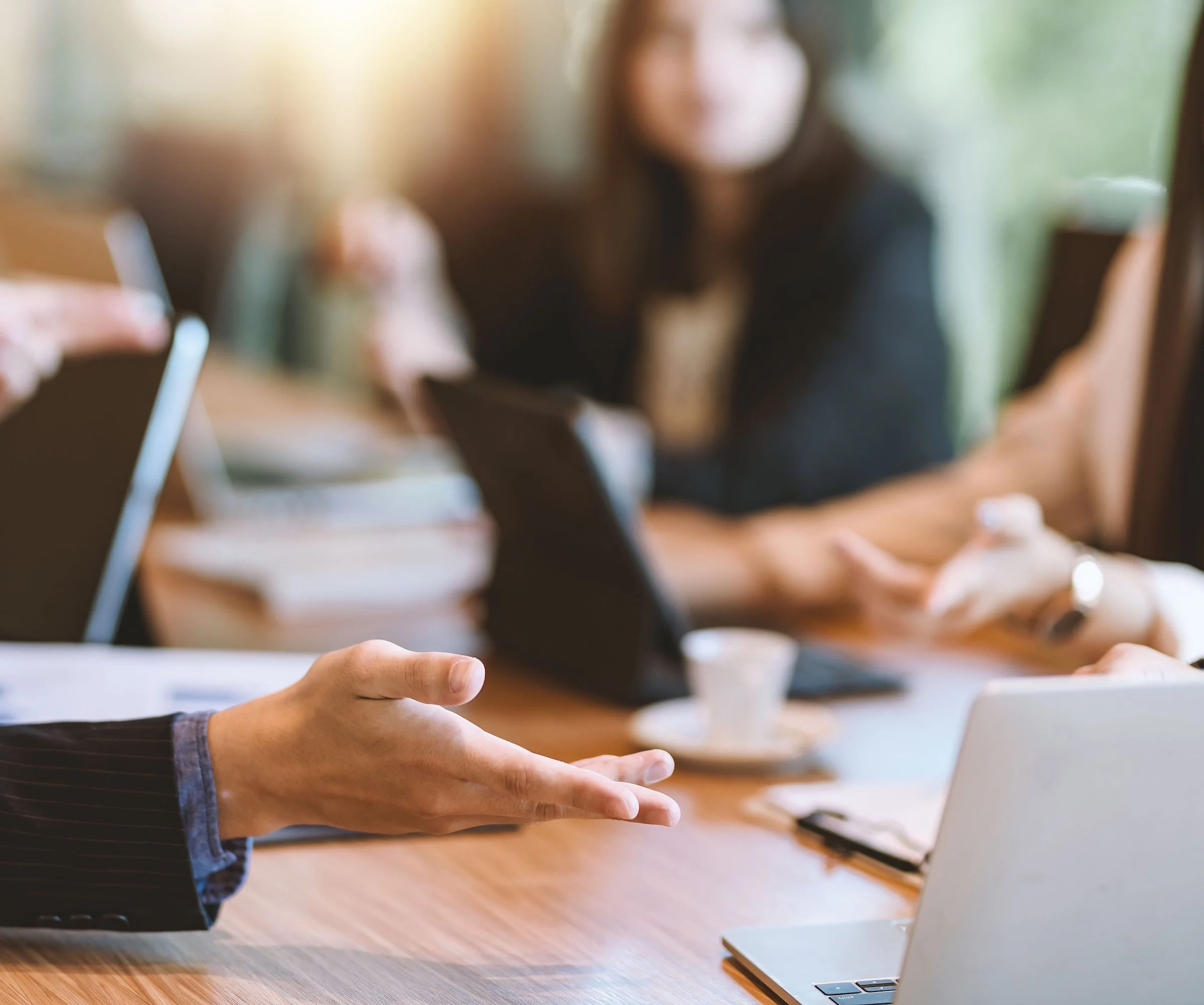 A person using a laptop in a meeting with another person, viewed in a blurred background.