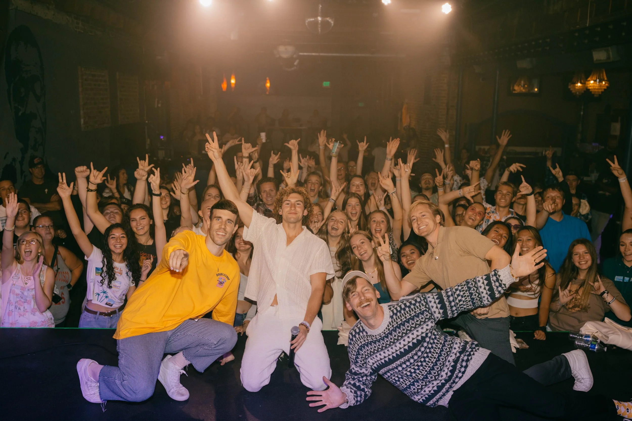 A group photo of the the band DOUBLE CAMP with the crowd after a concert, smiling and raising their hands.