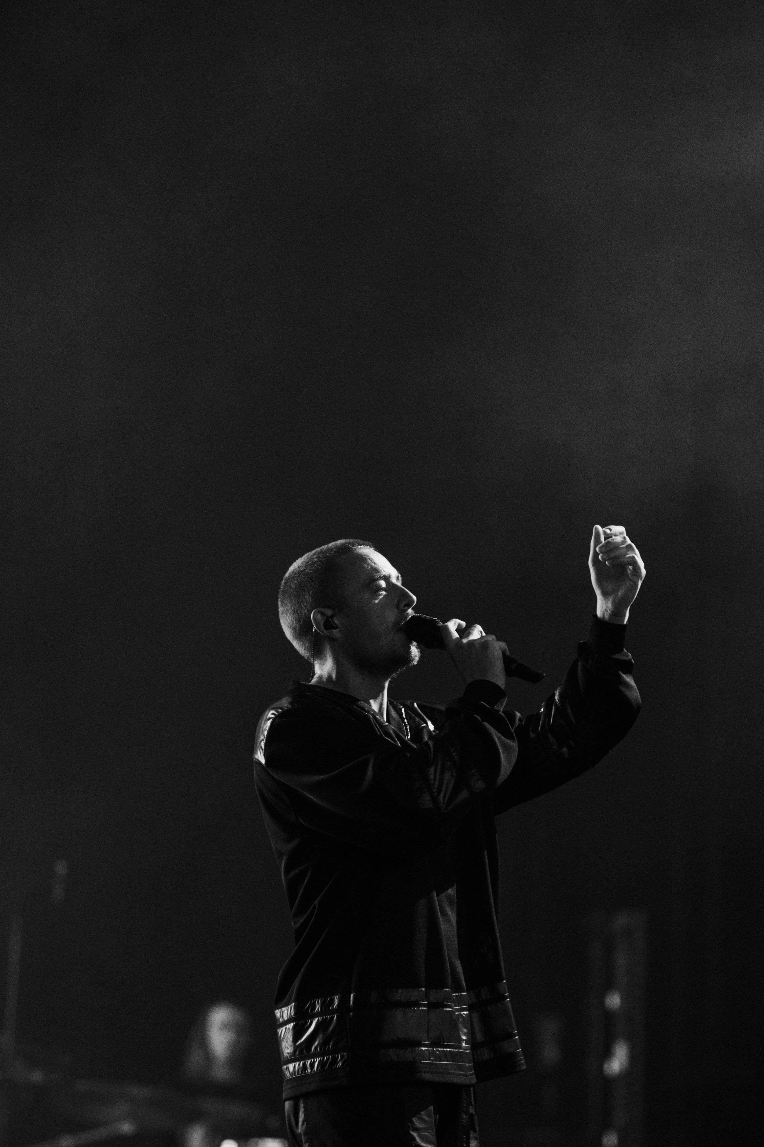A black and white photo of Dermot Kennedy performing live with his right fist raised, on a dark stage.