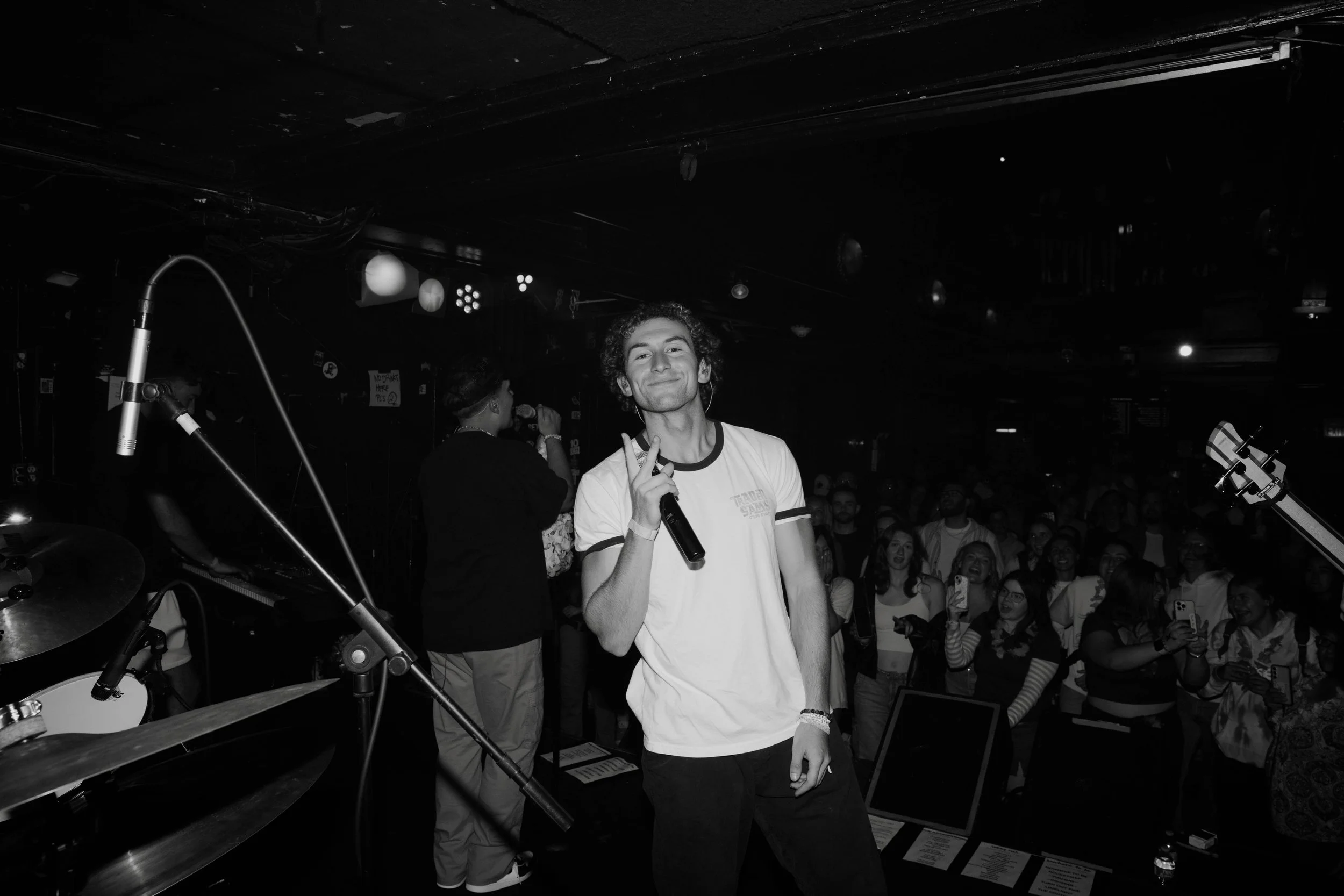 The musician Sammy Rash on stage holding a microphone, smiling, with a crowd of people in the background at a concert performing.