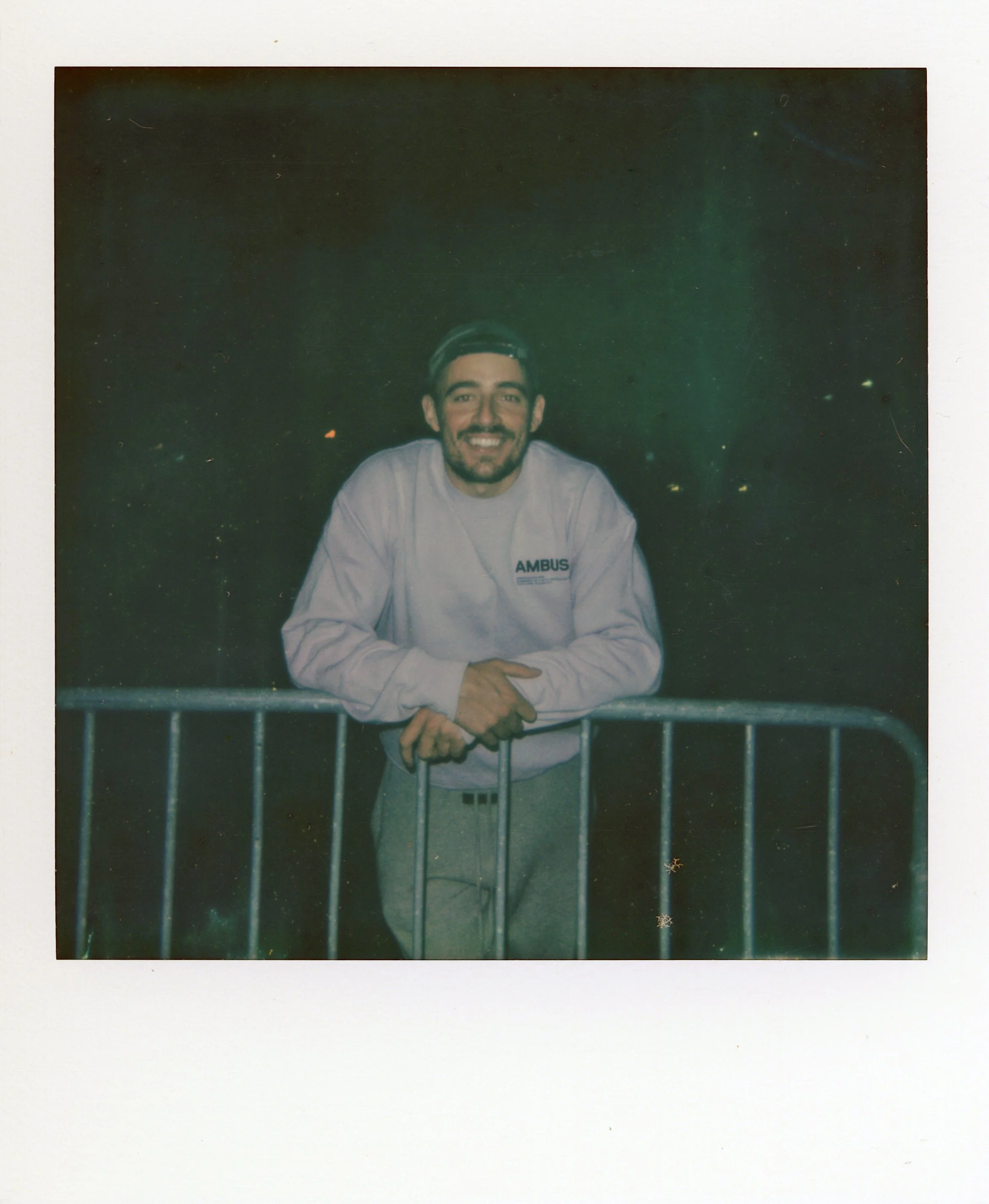 Polaroid photo of Dermot Kennedy after the show. He is leaning on a metal barricade, wearing a light-colored sweatshirt with a dark background.