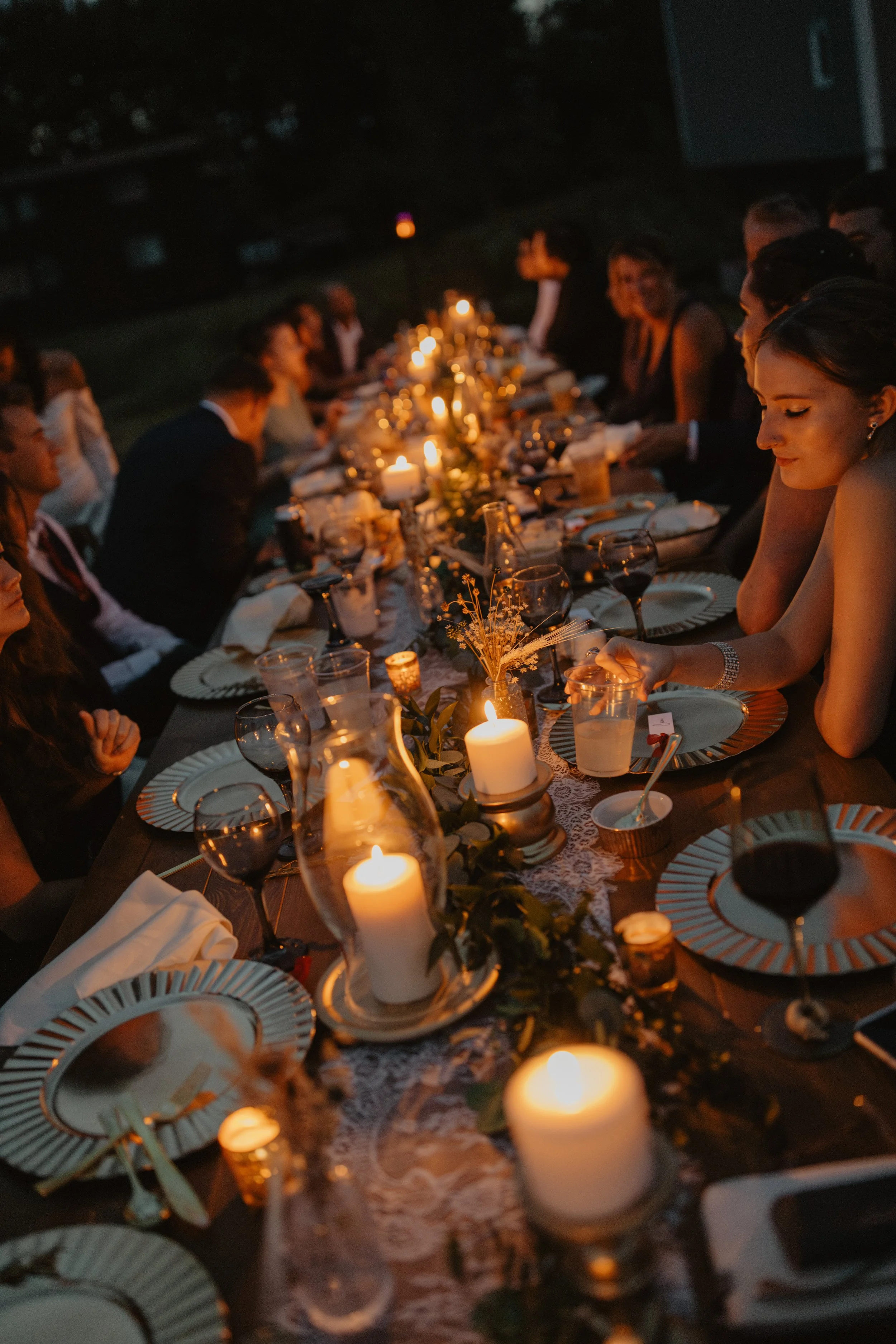 People gathered around a long, candlelit dinner table outdoors at night for a celebration or formal event.