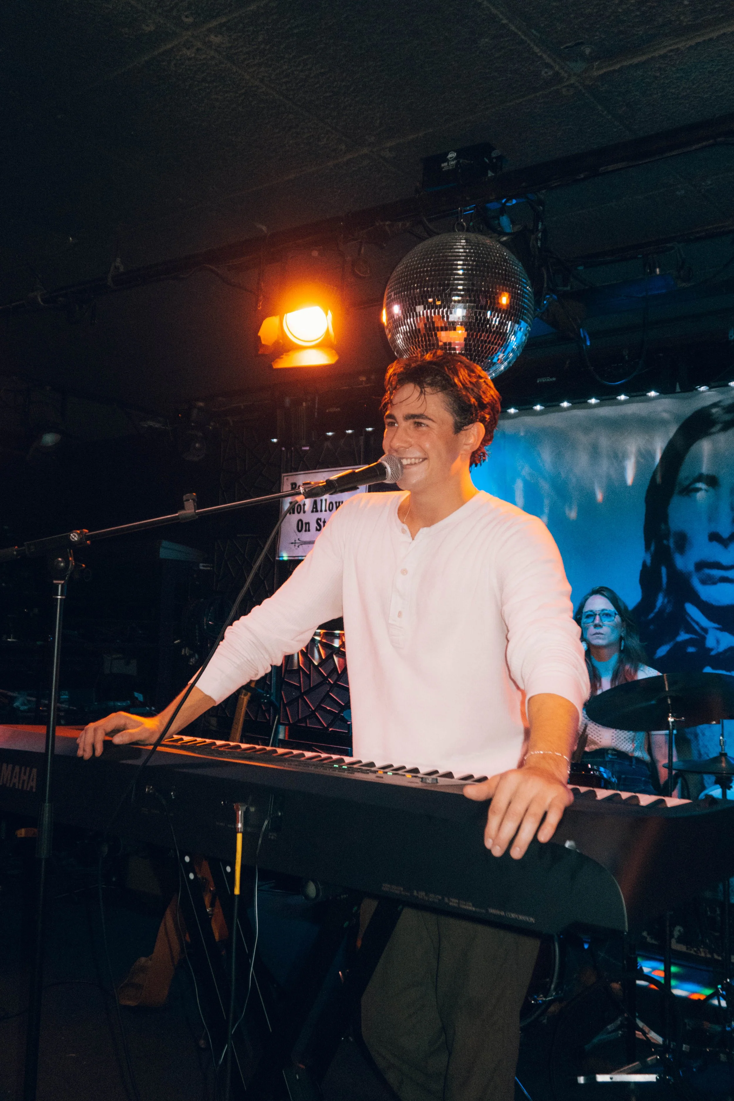 The music artist, Kaleb Cohen,  smiling and playing a keyboard on stage in Long Island, New York.