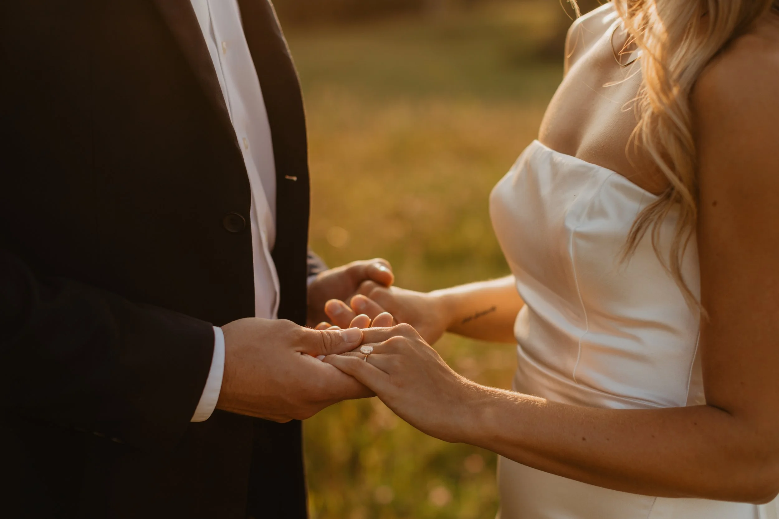 A couple holding hands during their wedding ceremony, with a focus on their hands and upper bodies.