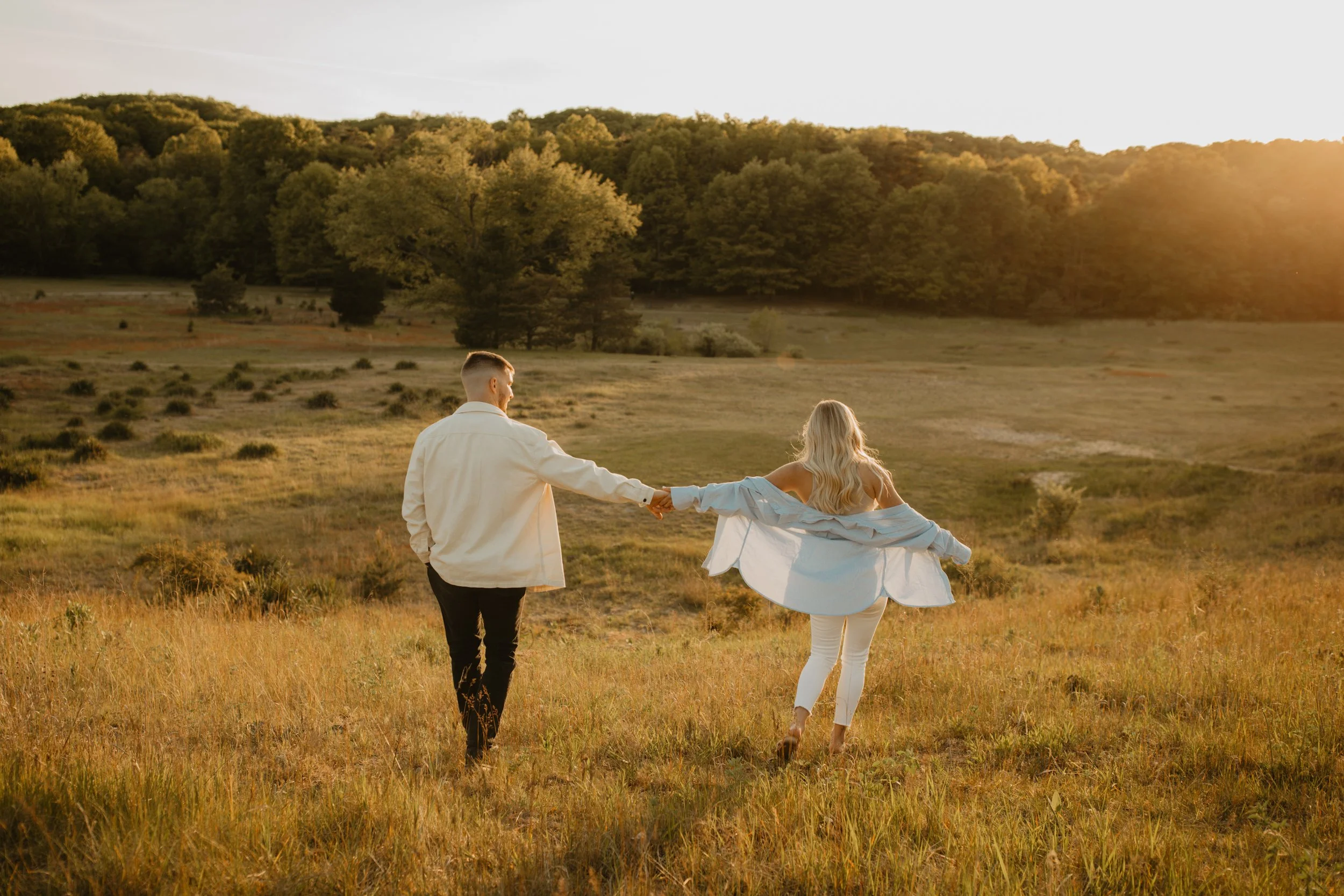 A couple holding hands as they walk through a grassy field during sunset.