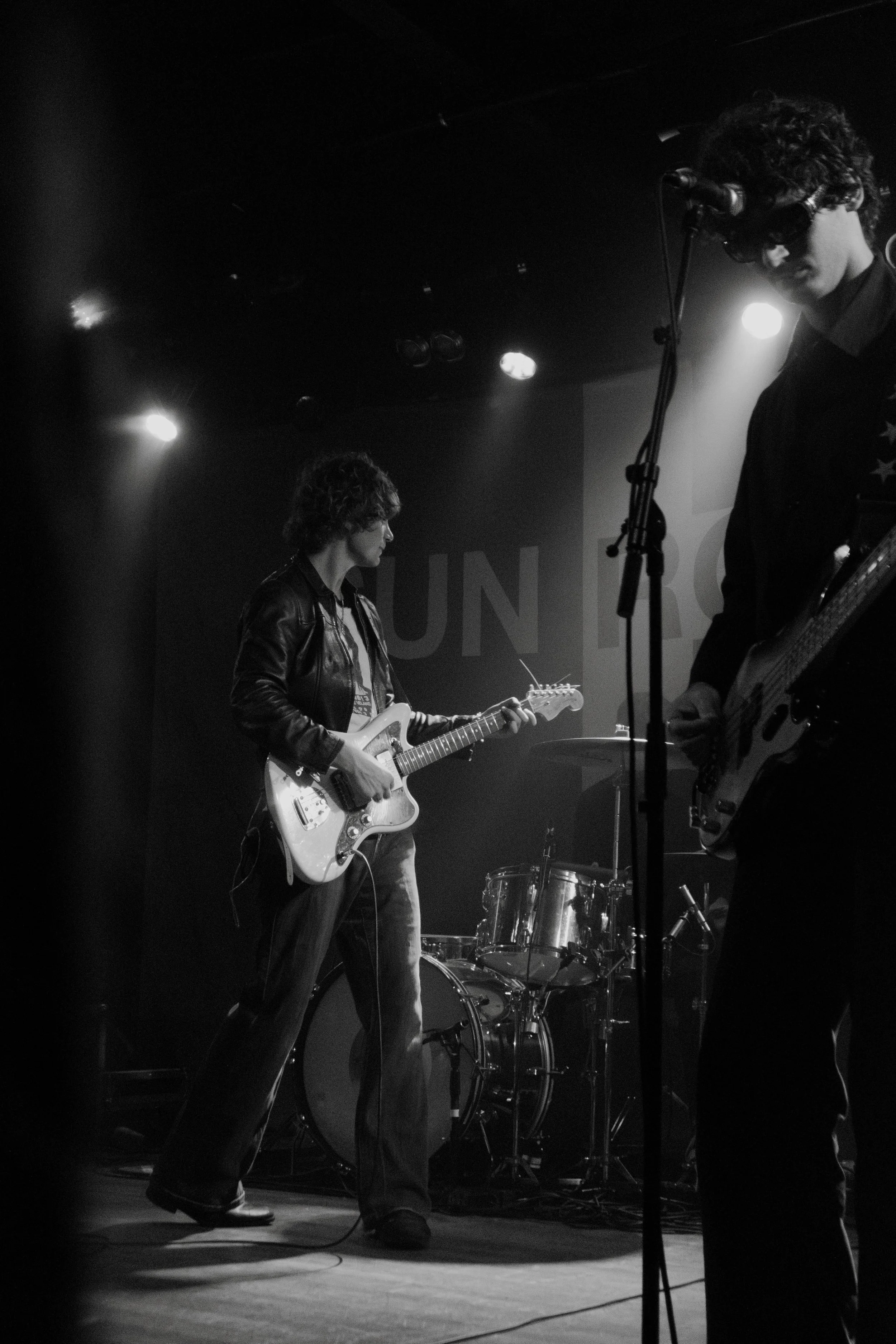 Black and white photo the band SUNROOM playing guitars on stage during a concert, with drums visible in the background in Chicago.