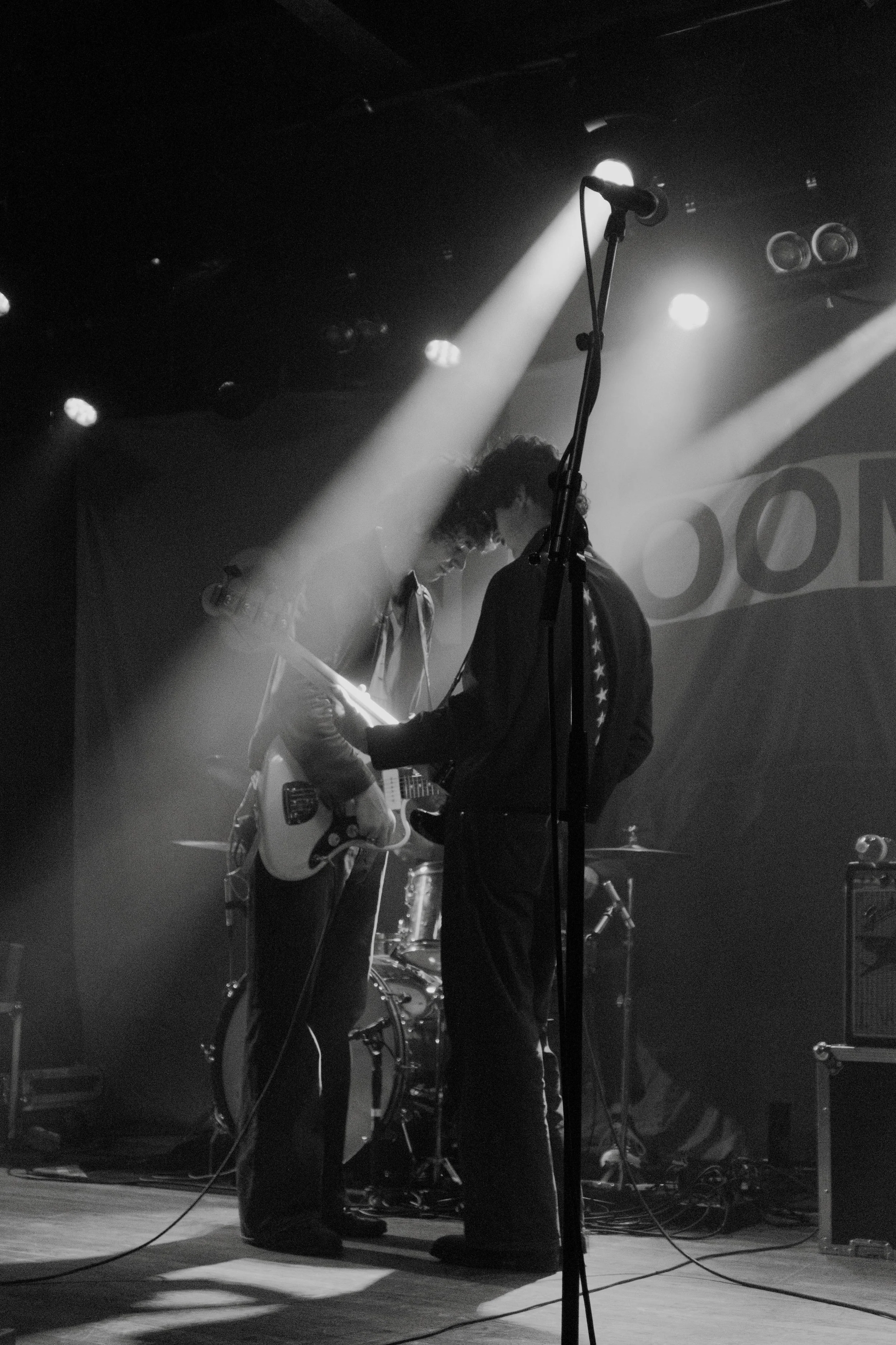 The band SUNROOM on stage with a guitar, illuminated by stage lights, in a black-and-white photo at a concert in Chicago