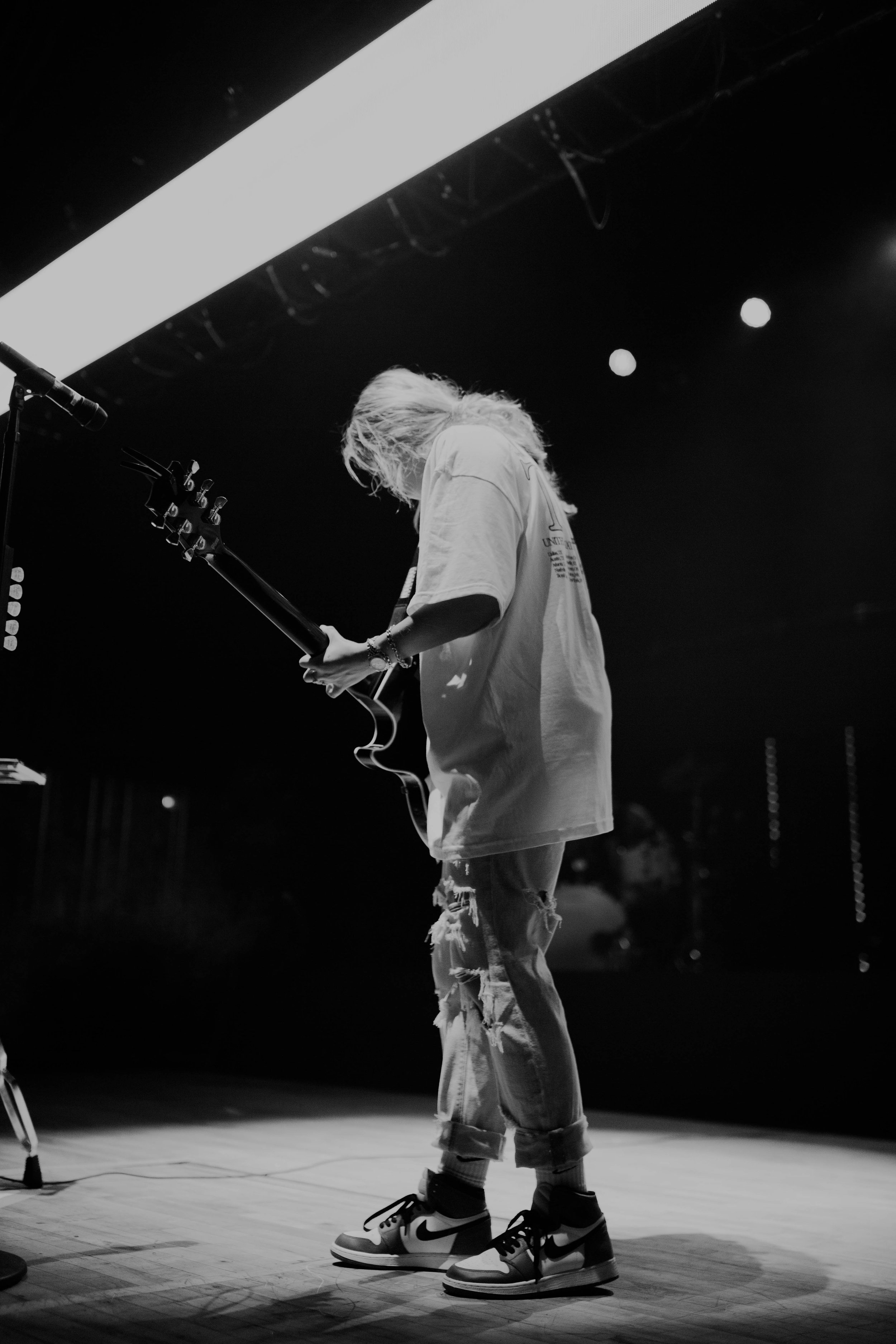 Chelsea Cutler plays an electric guitar on stage with stage lights overhead, black and white photo in Detroit, Michigan.
