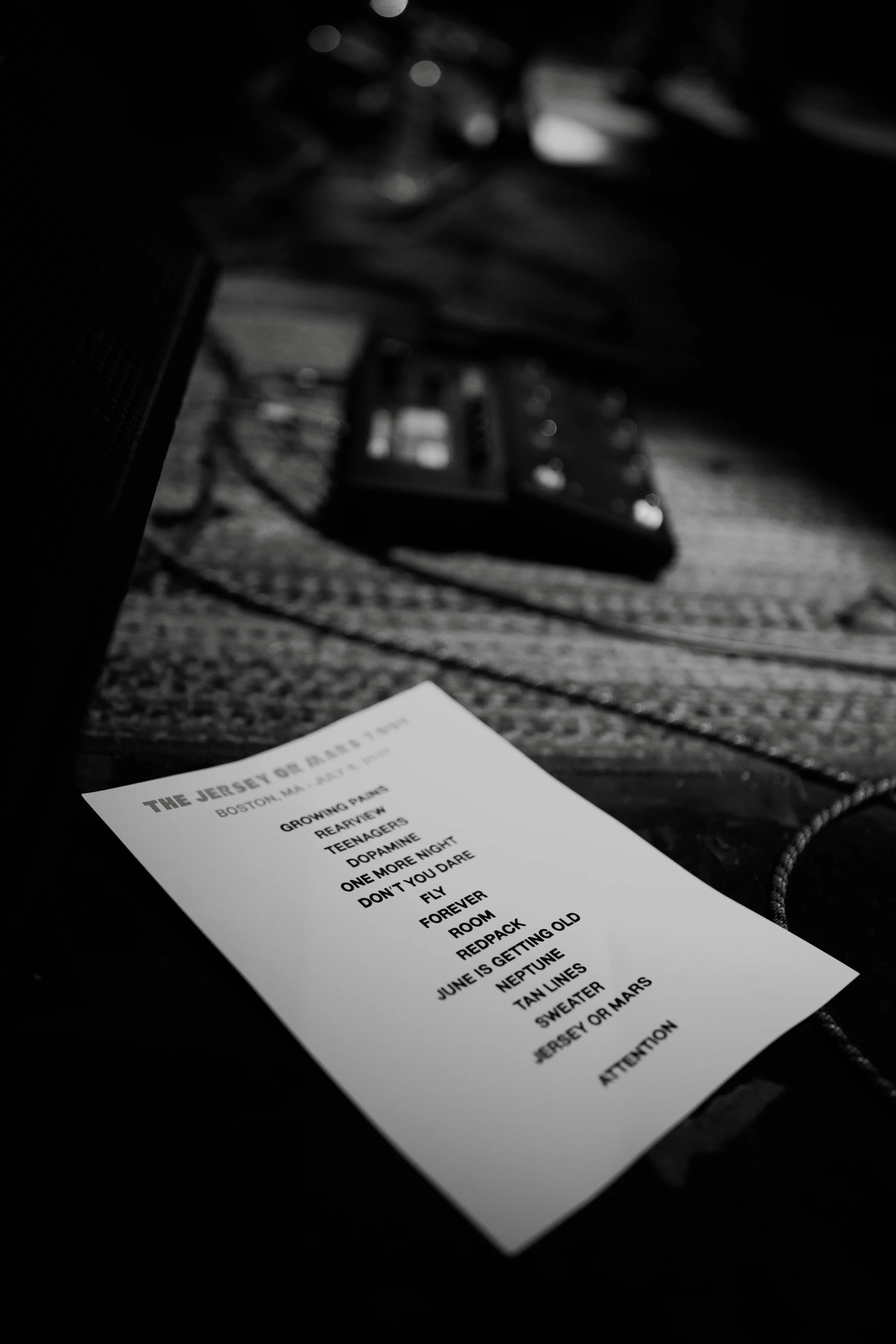 A printed setlist for Kevian Kramer's Tour  titled 'The Jersey or Mars Tour' resting on a textured surface, with some electronic equipment and cables in the blurred background.
