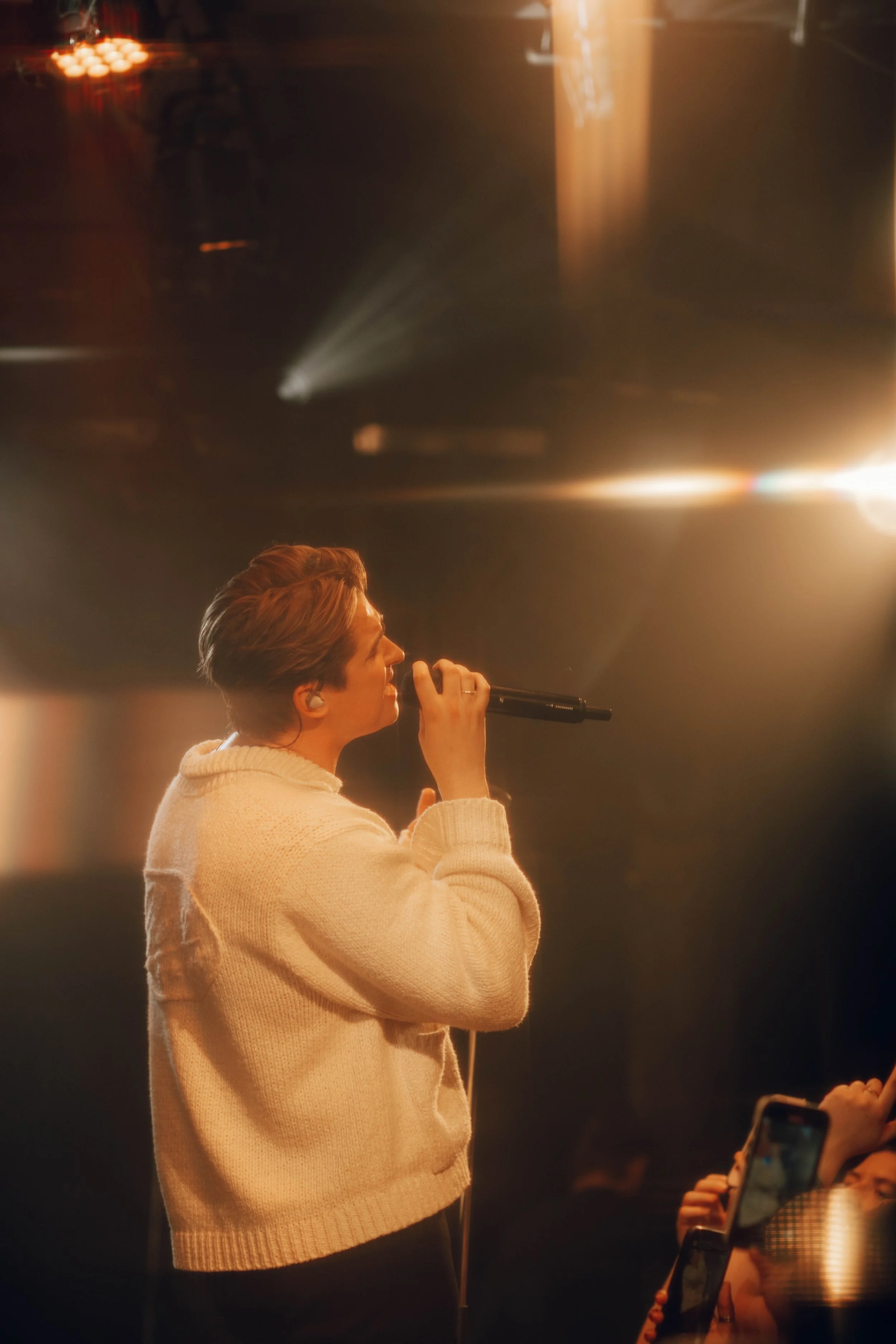 The musician Nicky Youre singing into a microphone on stage with warm lighting.