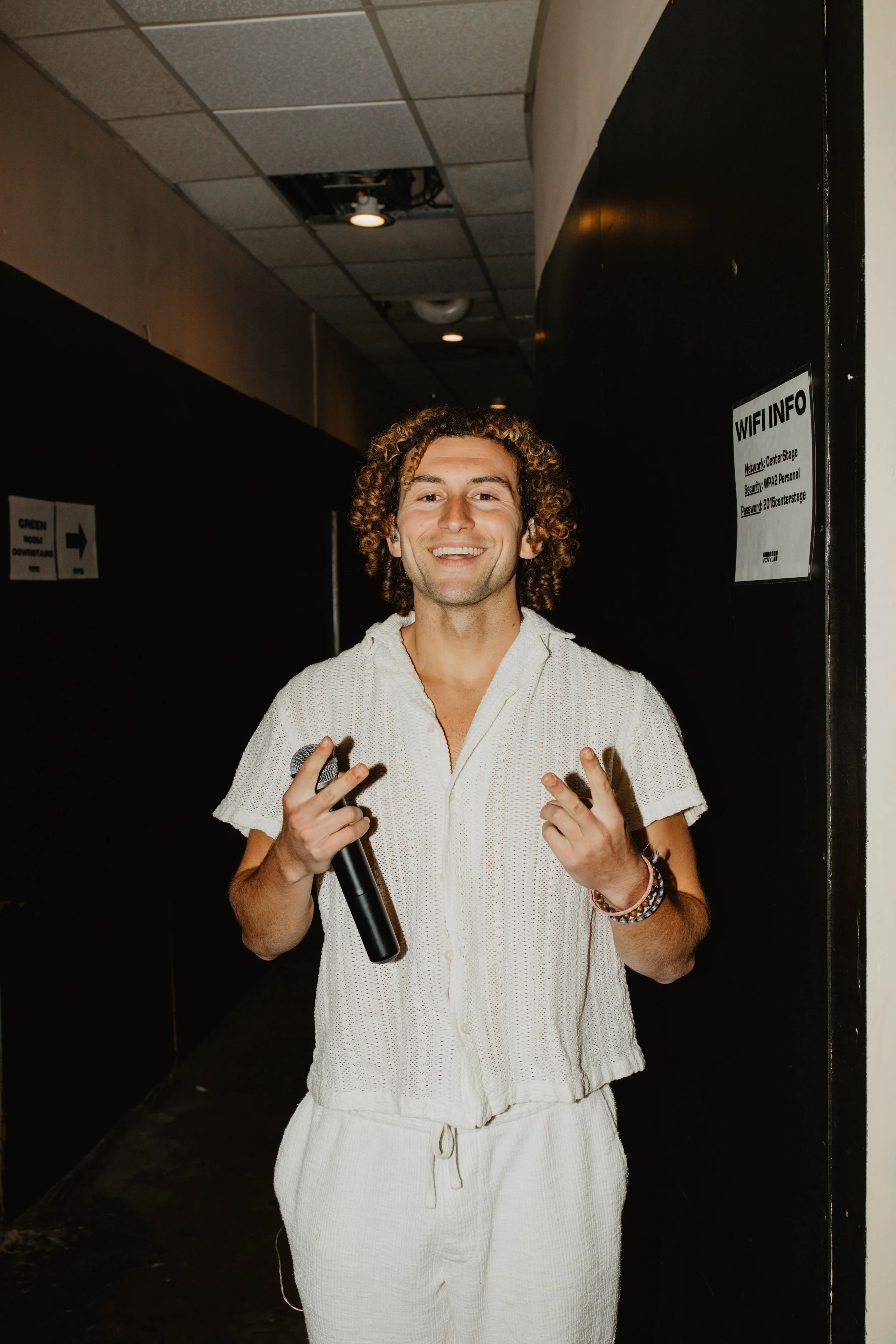 Sammy Rash before he goes on stage, smiling, holding a microphone in his right hand, standing in a hallway.