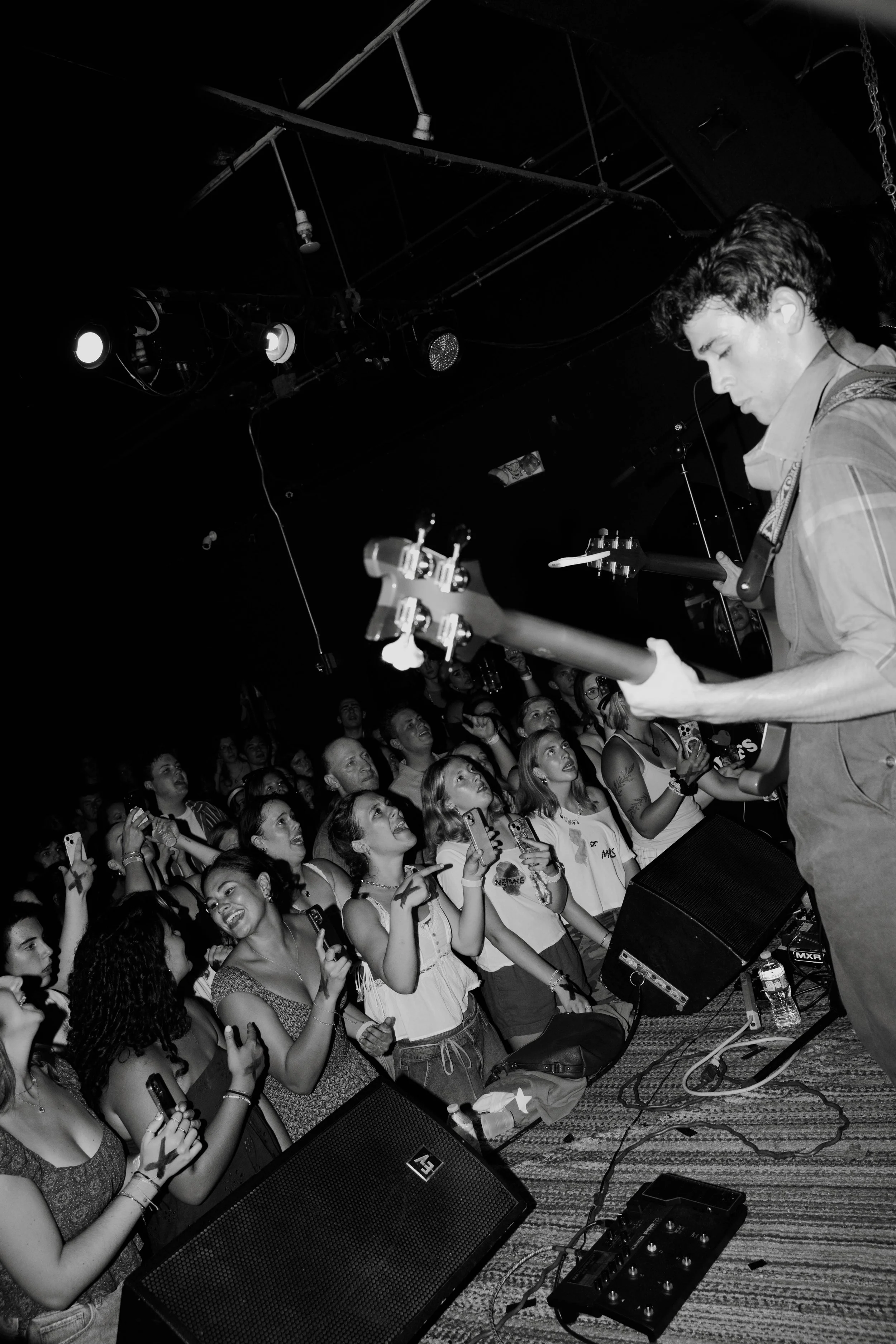 Black and white photo of Kevian Kramer's guitarist performing on stage with a crowd of young women cheering and recording with their phones.