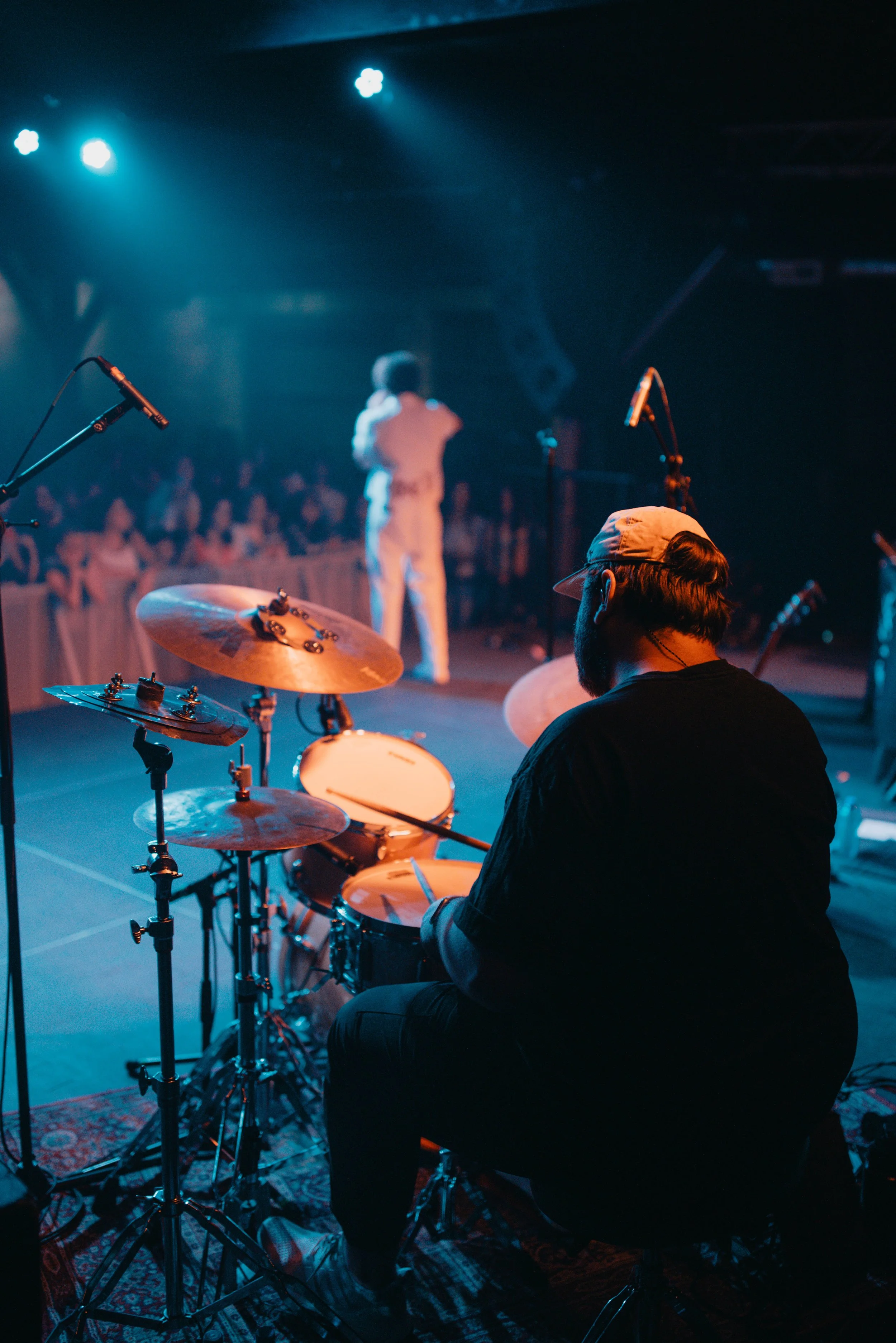 Sammy Rash's band member playing drums on stage during a concert with a singer in the background and an audience watching.