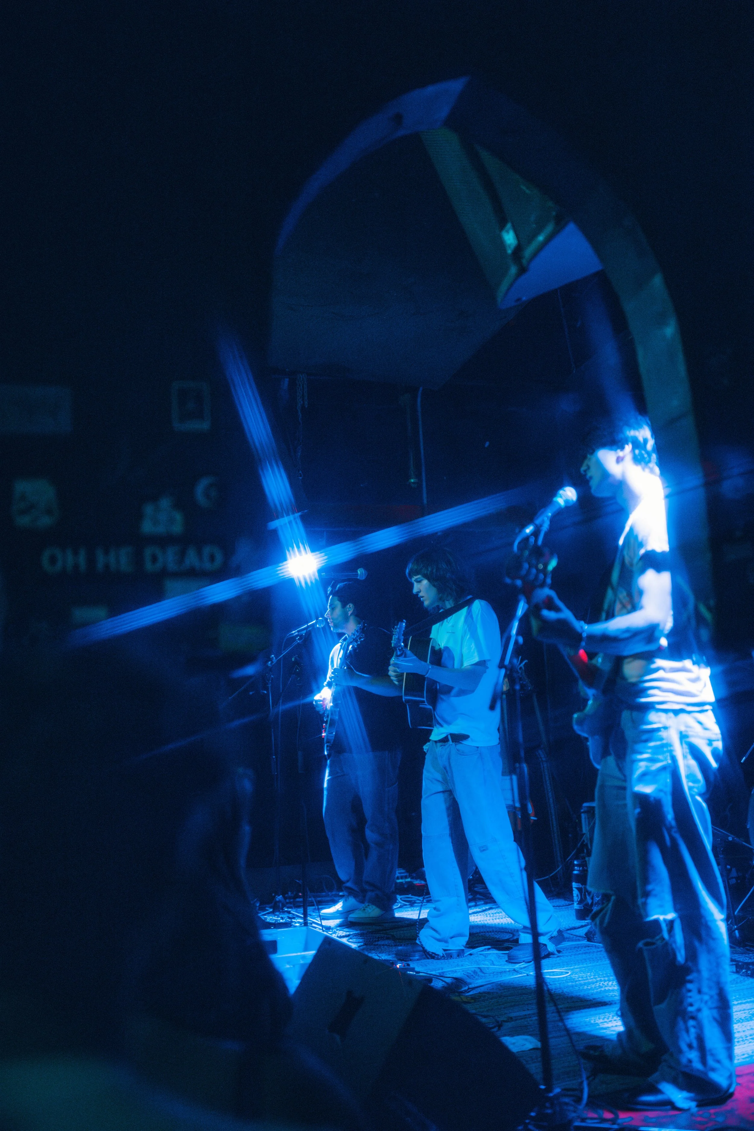 Dipsea Flower performing on stage under blue lighting, two playing guitars and one singing into a microphone in Boston.