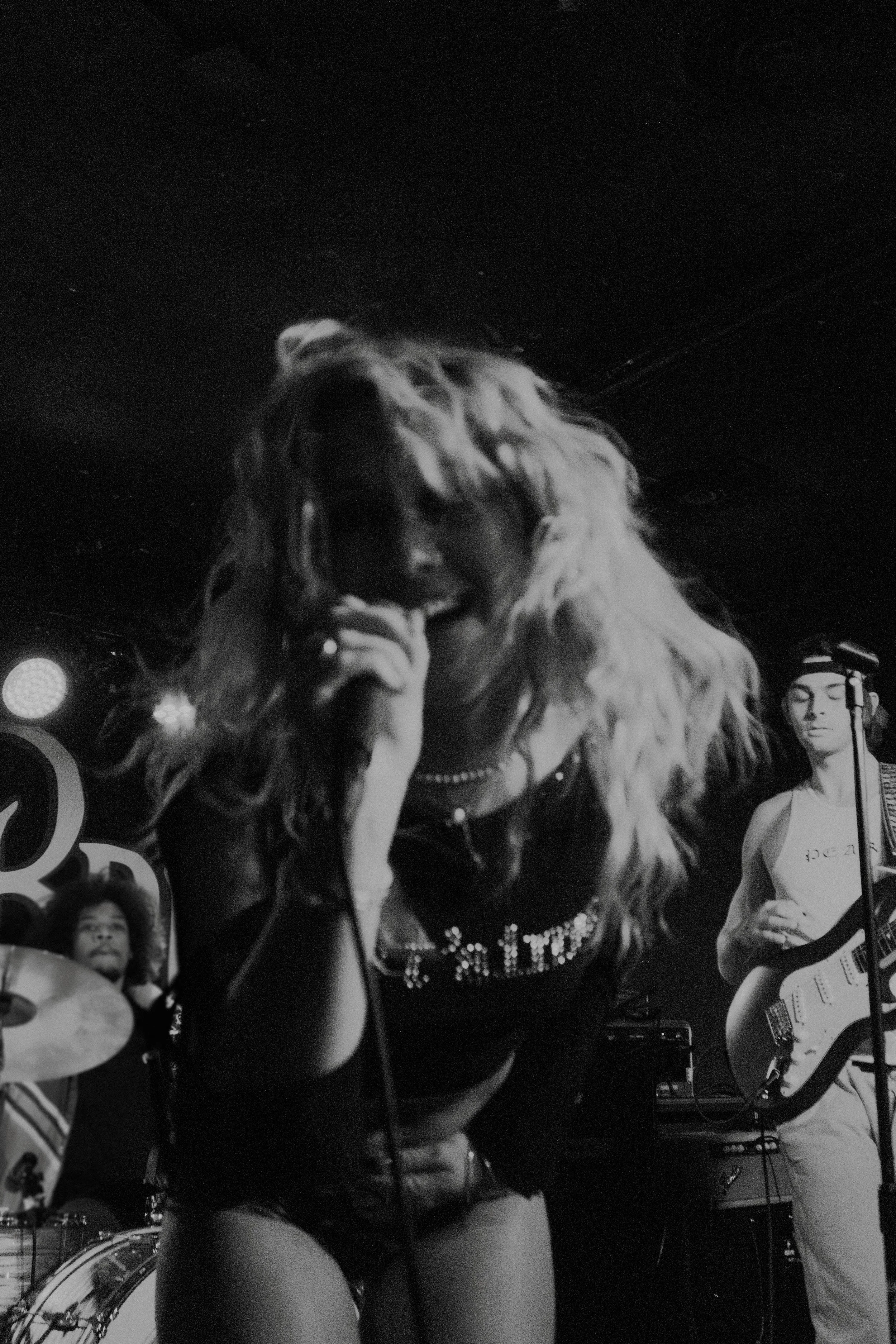 Music artist called PEARL performing on stage with a band, including a drummer and guitarist, in black and white, in Detroit Michigan.