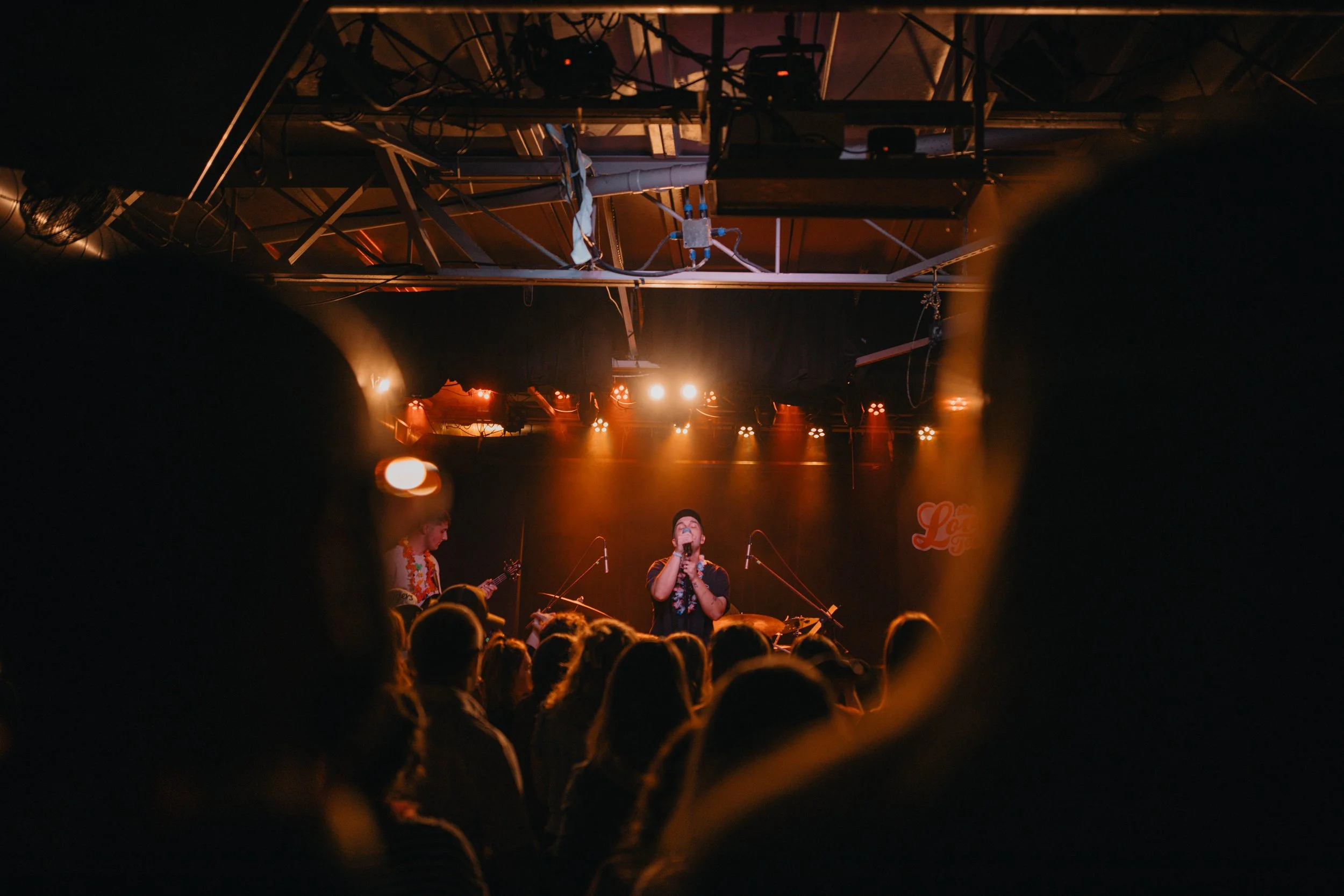 Live music performance on stage with the band The Astronomers, the, audience viewing through a heart-shaped opening, warm orange stage lights illuminating the scene.