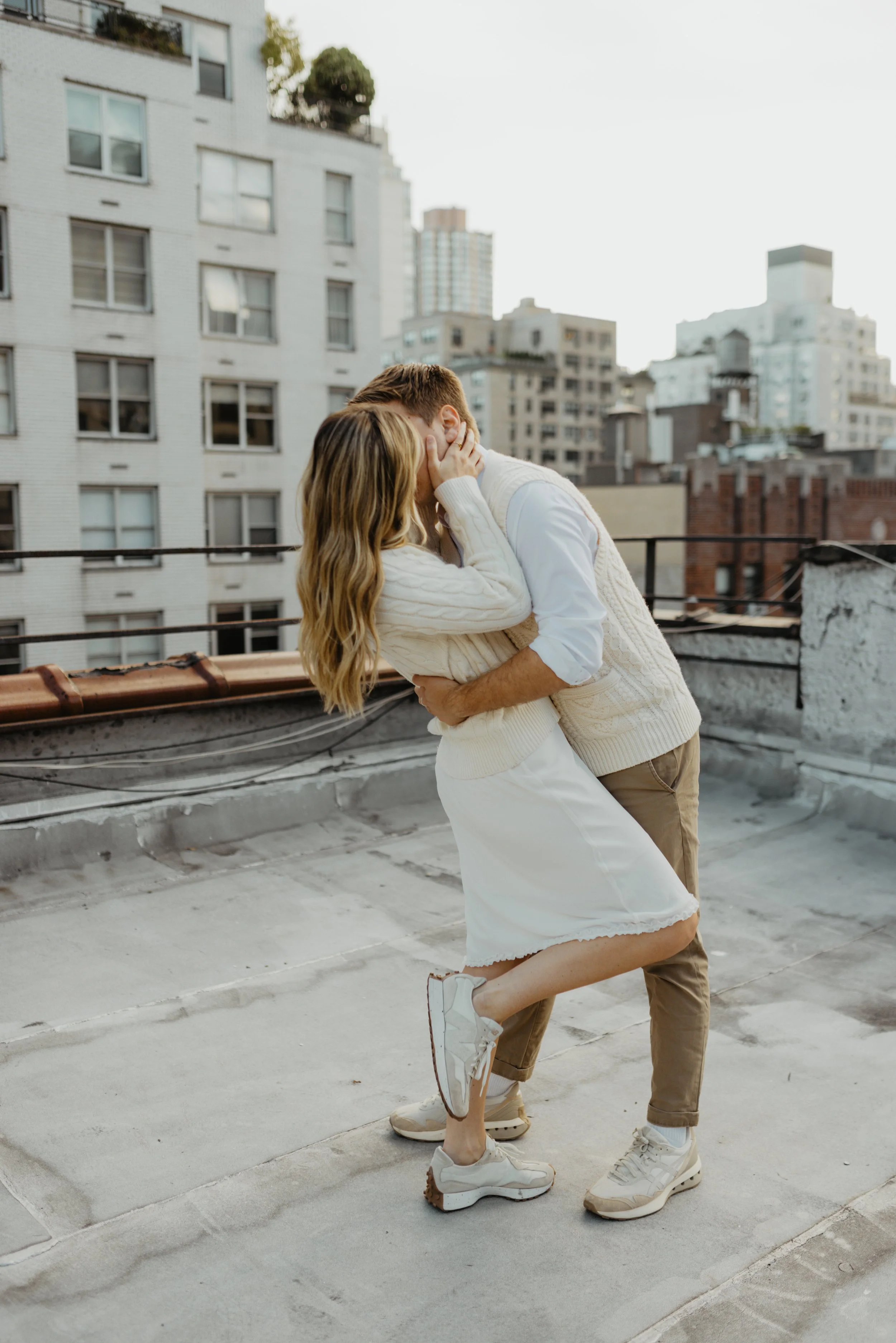 A couple kissing on a rooftop in an urban setting, with buildings in the background.