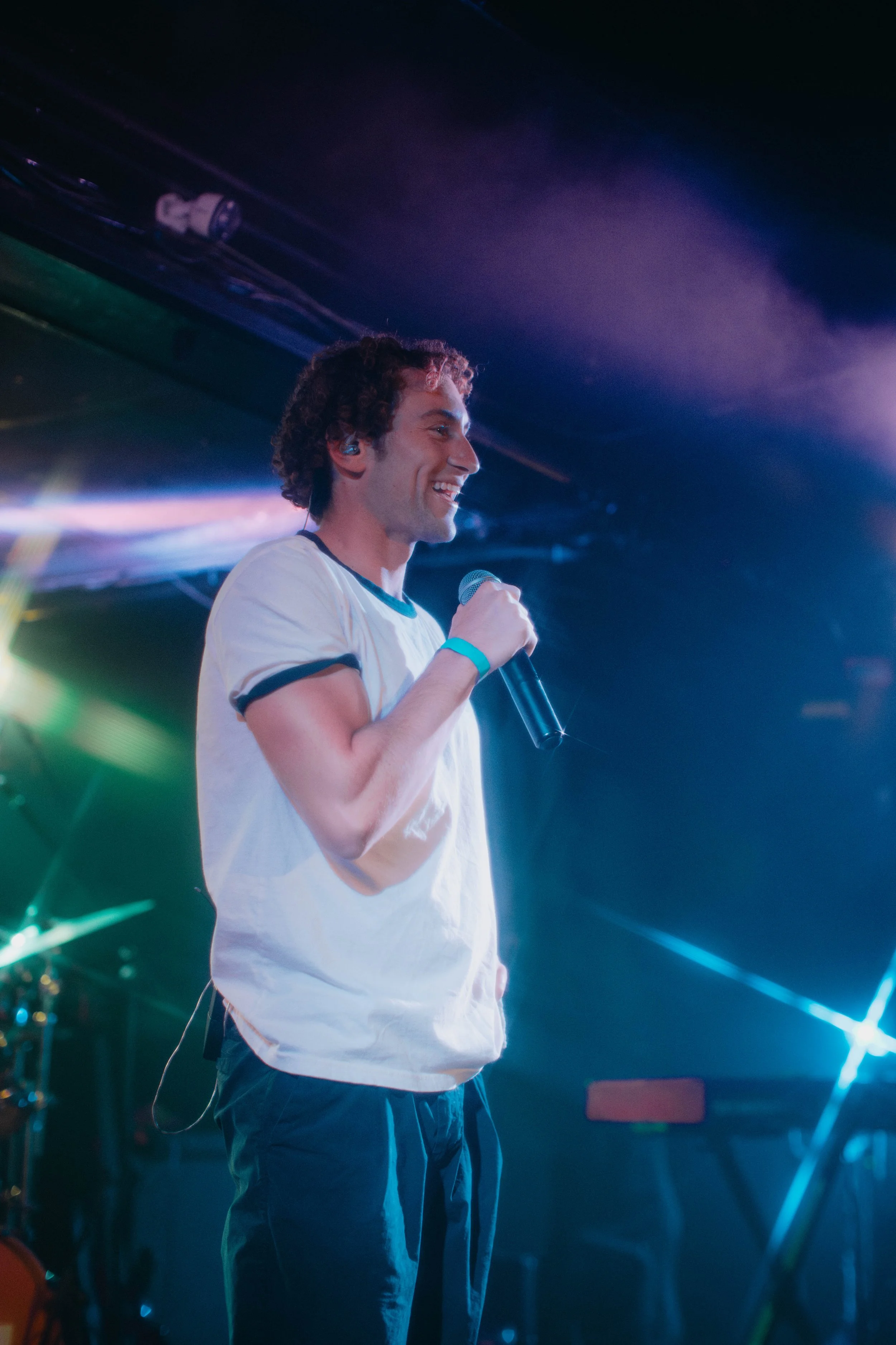 Sammy Rash holding a microphone on stage under colorful lights, performing at a live concert.