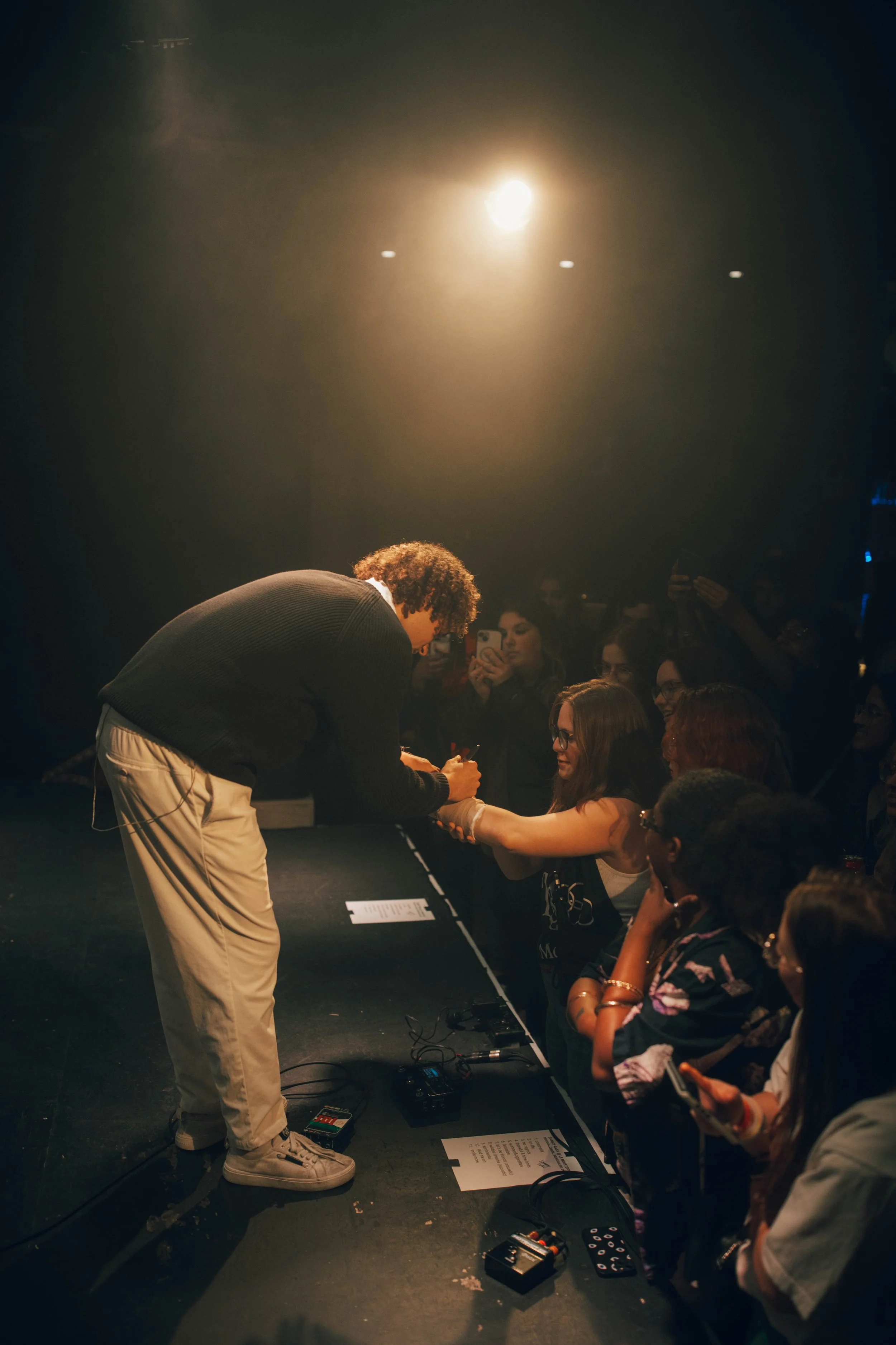 Sammy Rash on stage signing autographs for fans during a concert, with audience members reaching out and taking pictures in a dimly lit setting with bright overhead lighting.