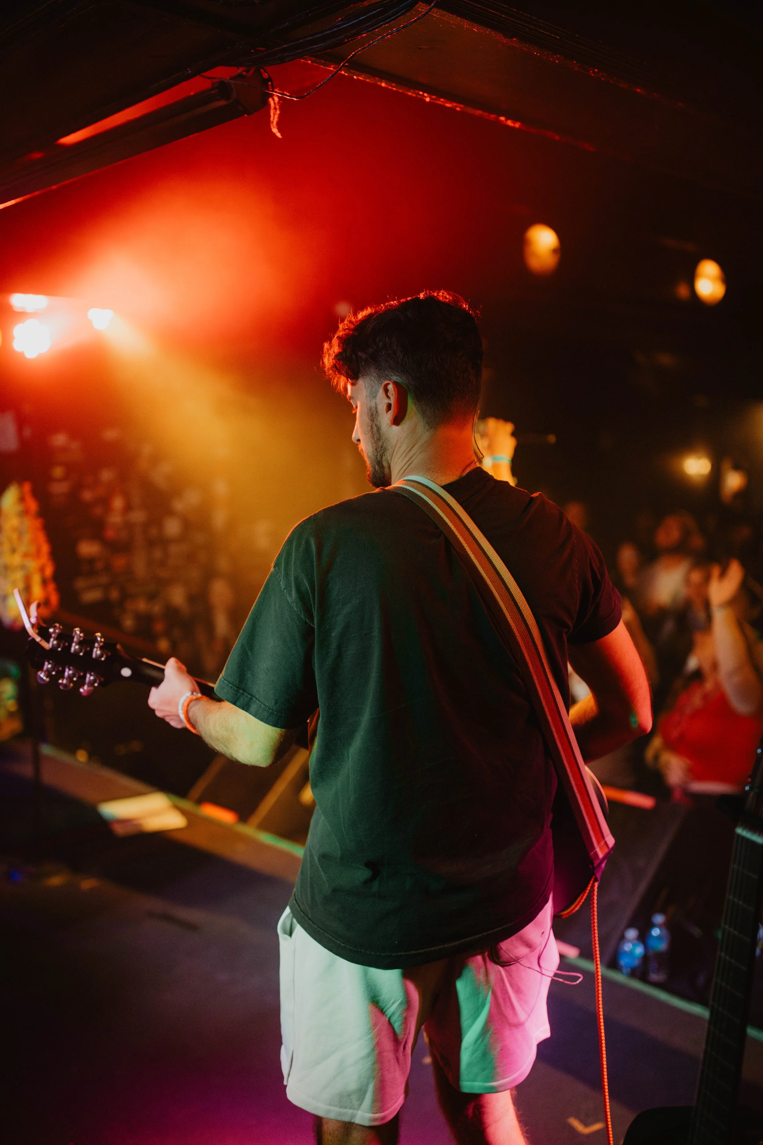 The band called,  The Astronomers playing an electric guitar on stage with colorful stage lights and a blurred audience in the background.