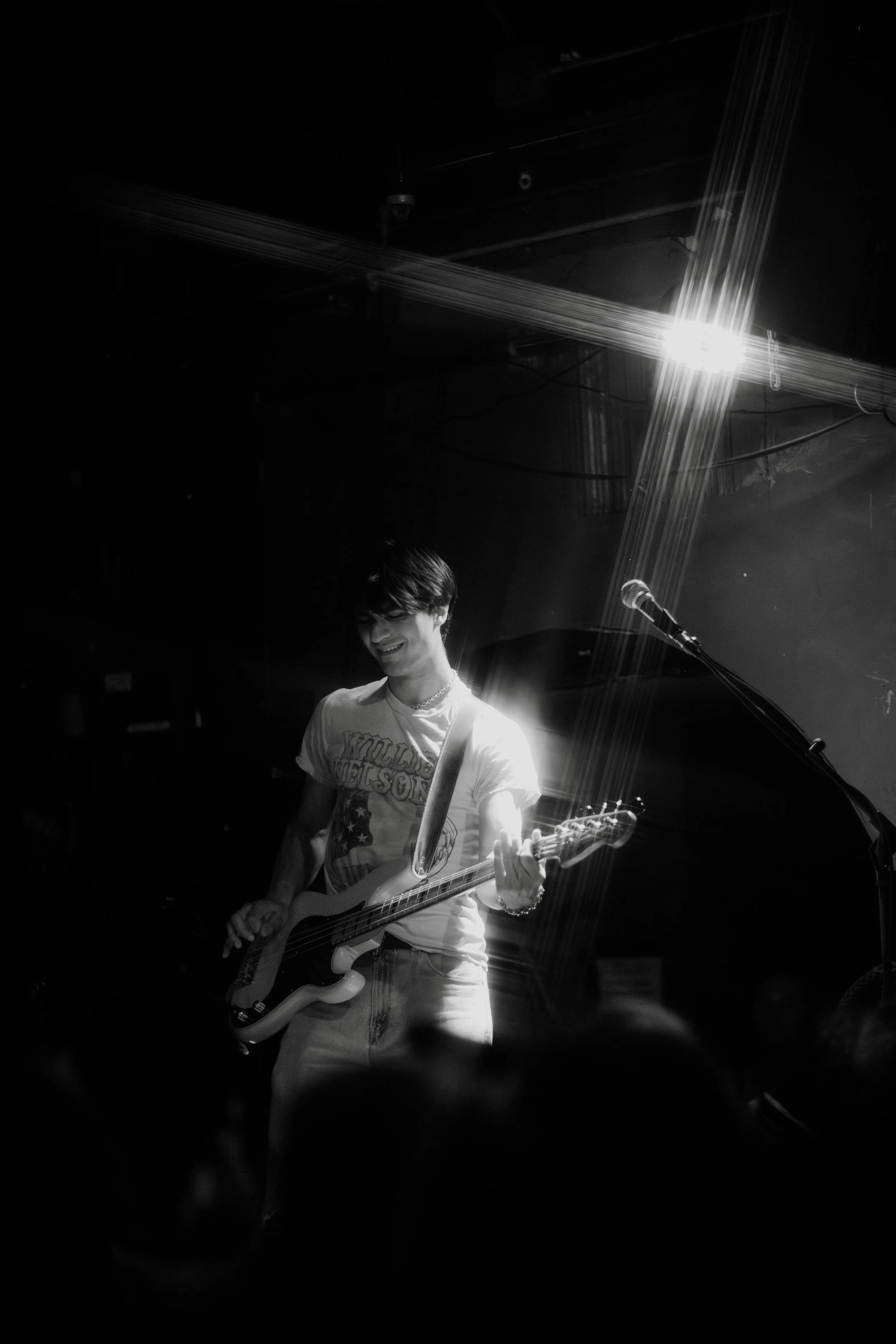Kevian Kramer's band playing guitar on stage with a bright spotlight overhead, black and white photo.
