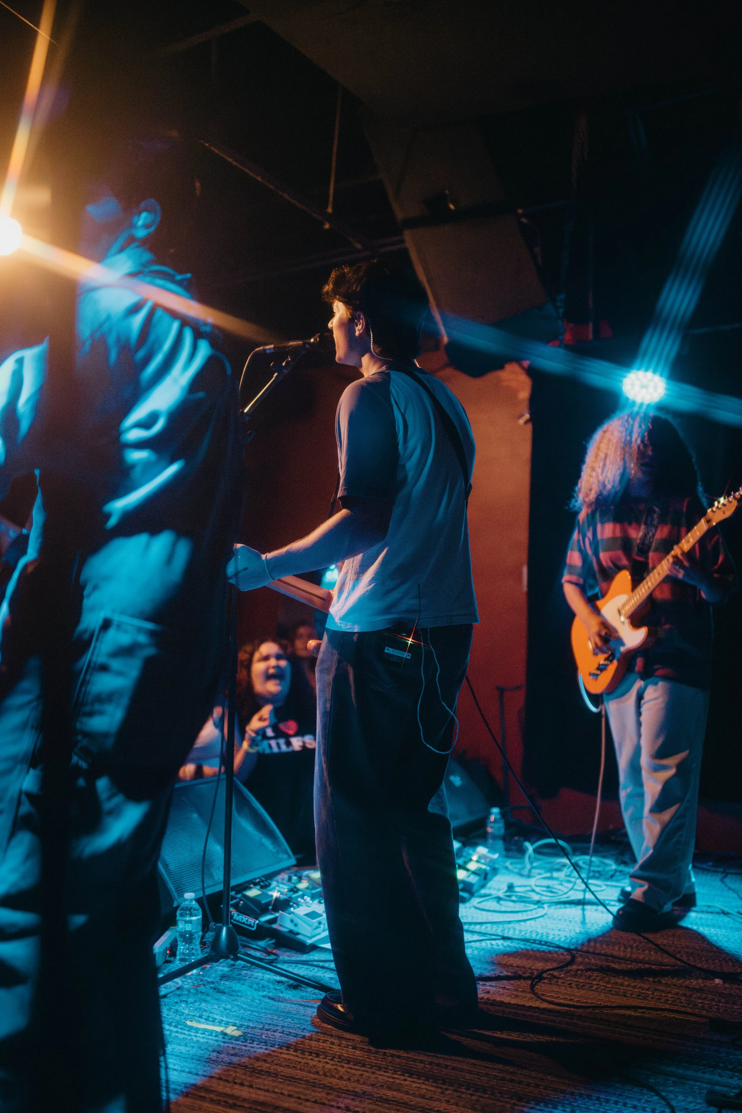 Kevian Kramer's band performing on stage with colorful lighting, focused on a female guitarist and a male vocalist.