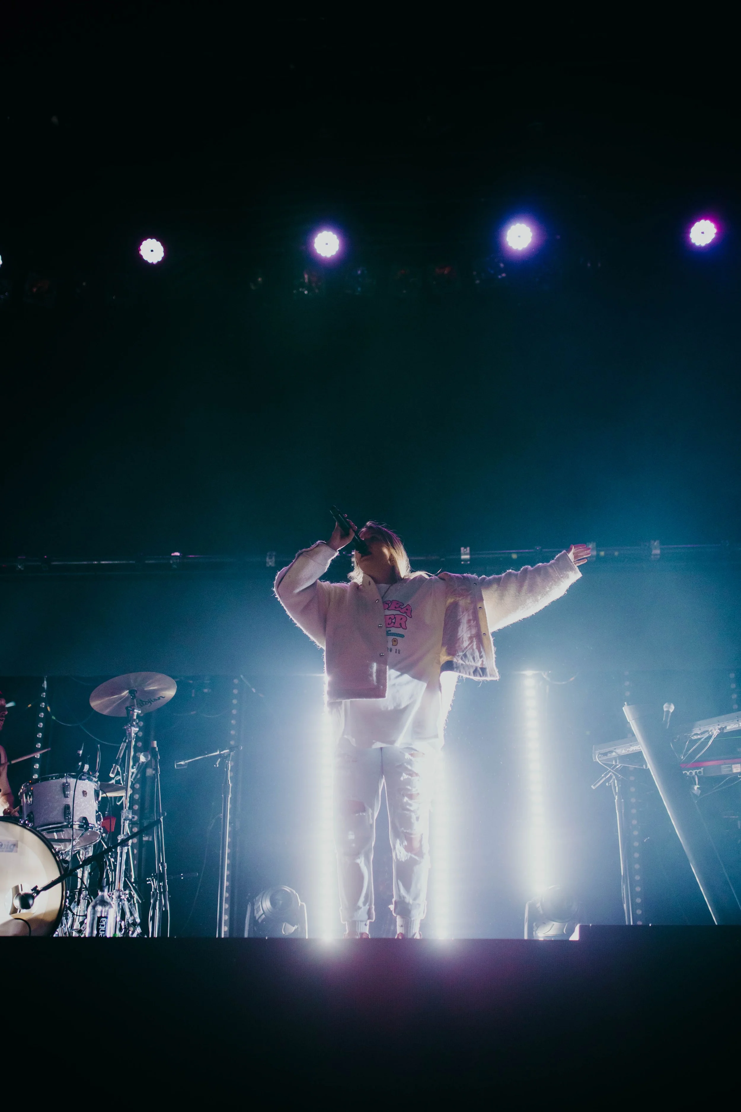 Chelsea Cutler performing stage with bright lights behind them, surrounded by musical instruments.