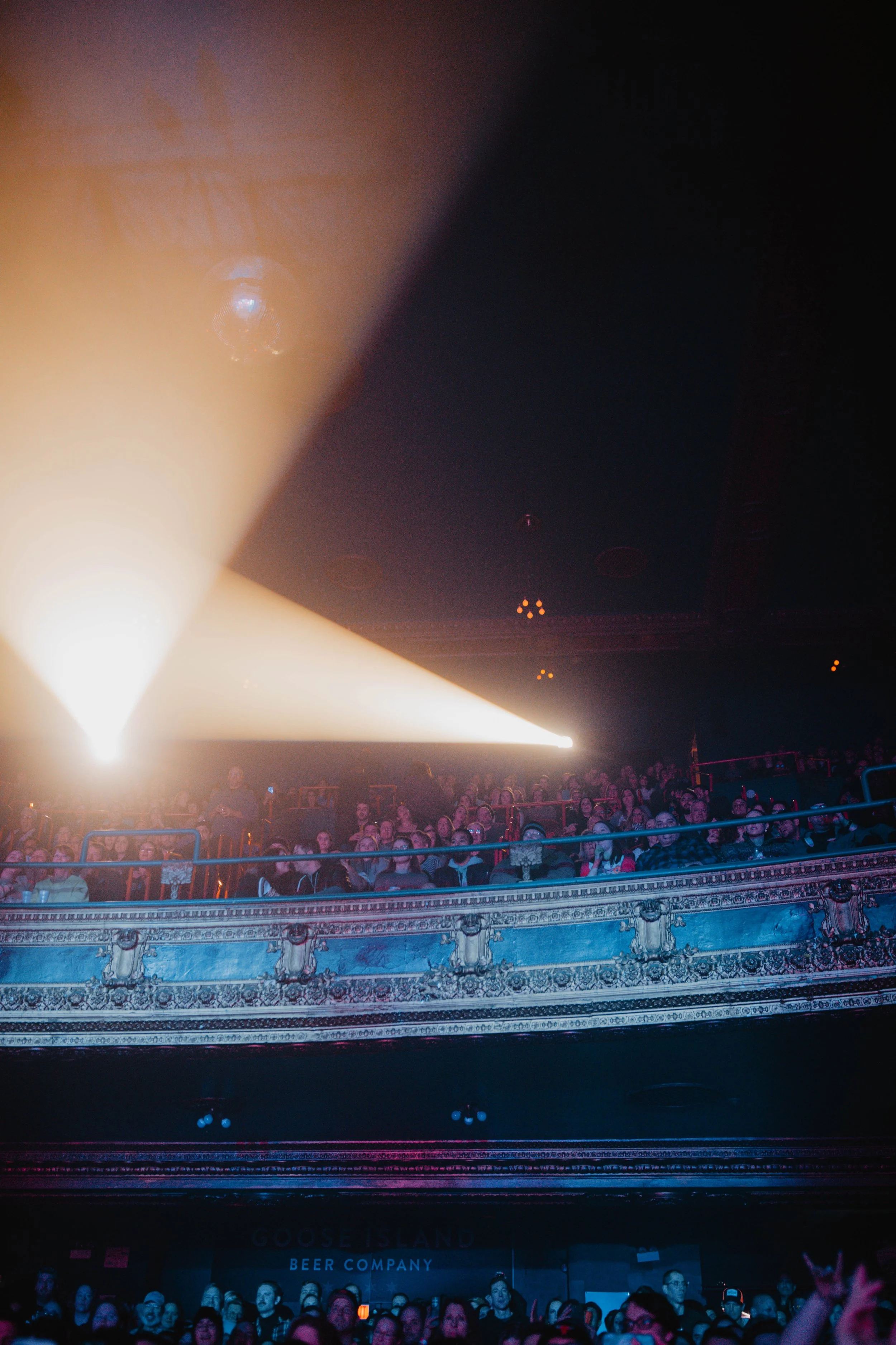 Crowd watching a concert or performance in a theater with ornate balconies, illuminated by stage lighting in Detroit, Michigan.
