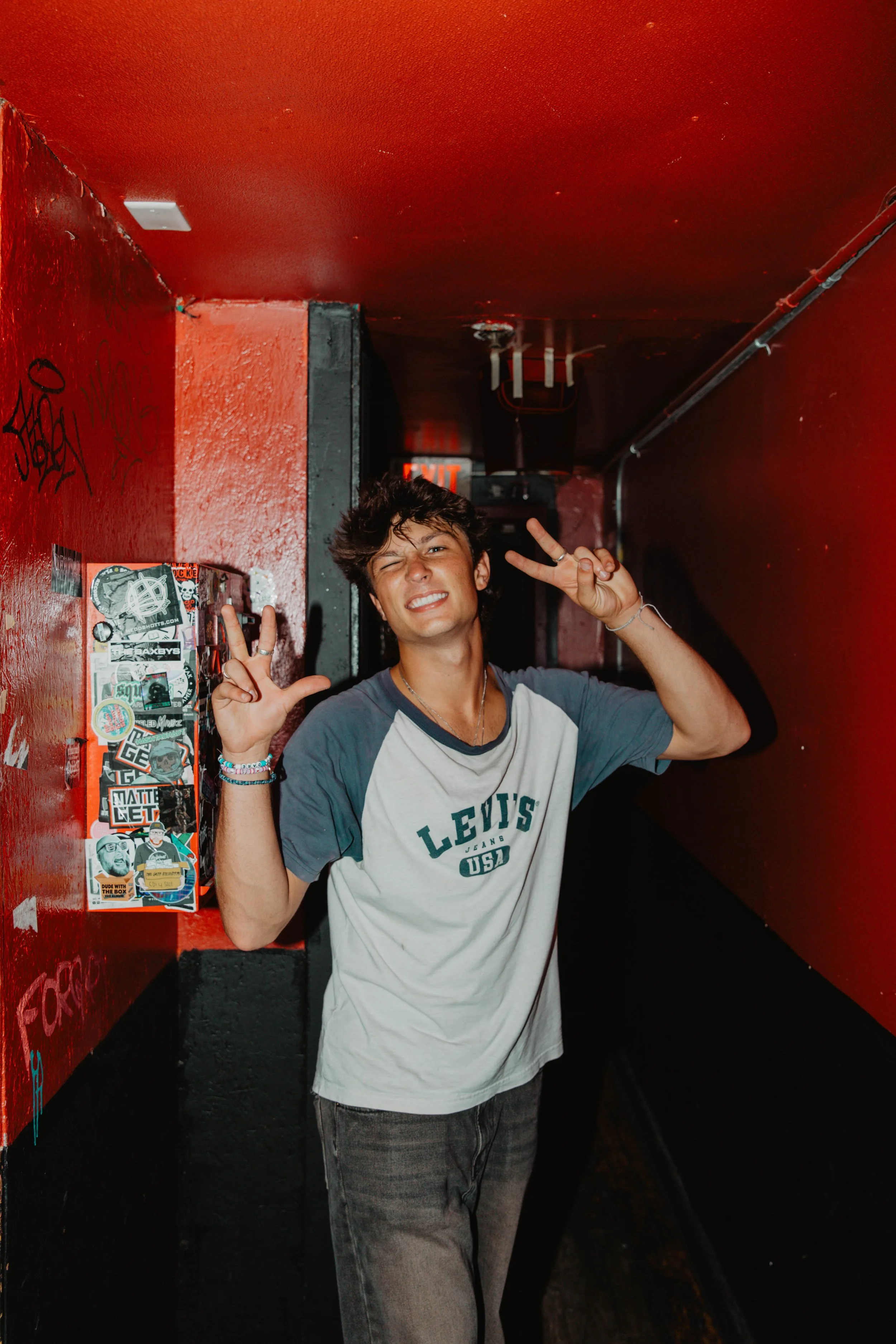 The music artist, Kevian Kramer, making peace signs, smiling at a music venue in Boston. 