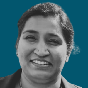 A woman smiling with a small nose piercing, dark hair, and a dark jacket, set against a solid teal background.