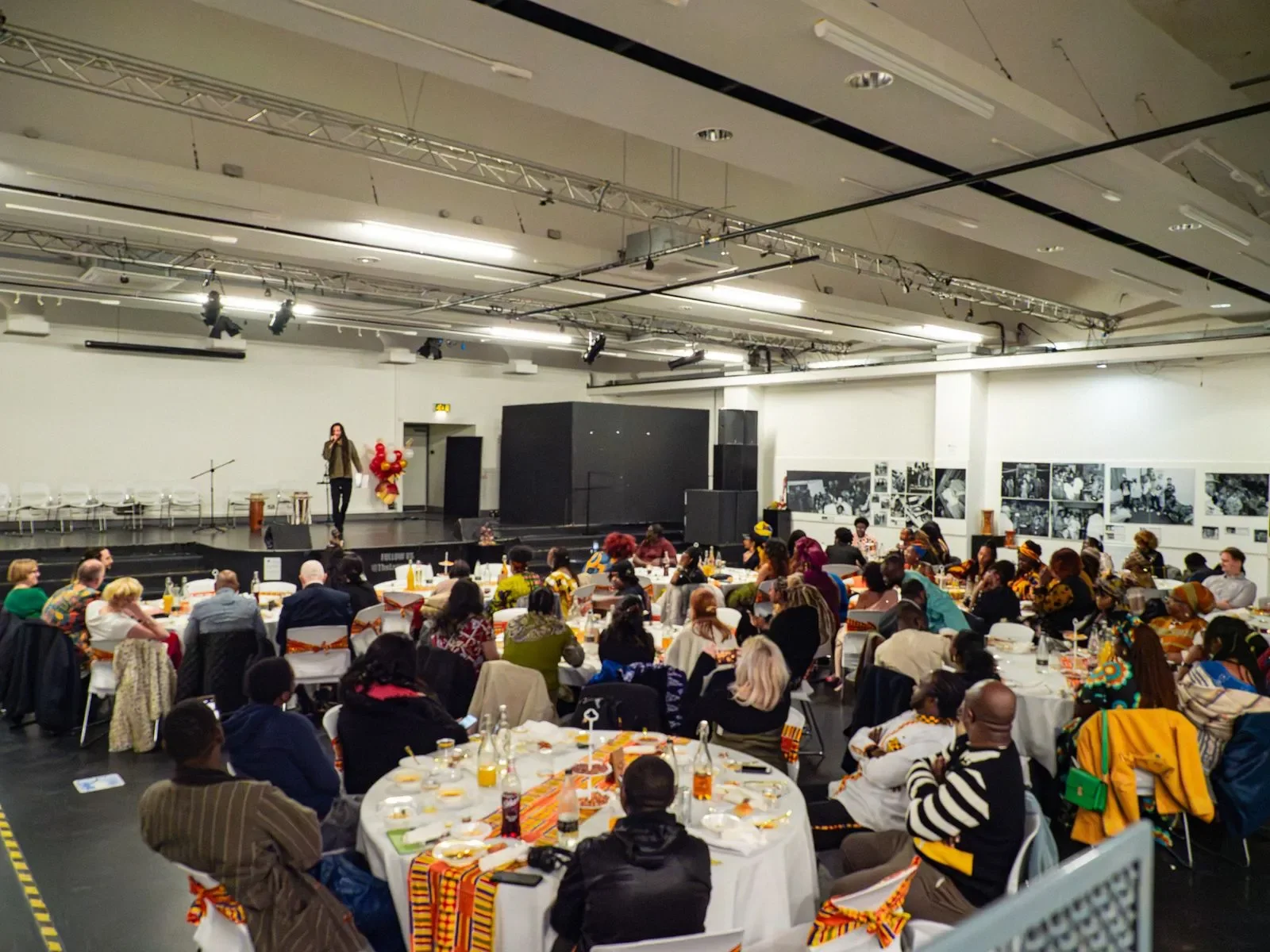 A photo from a community event with a man on stage talking to a crowd of people sitting at tables