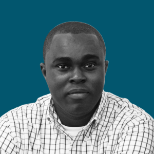 Portrait of a young man with short hair, wearing a checkered shirt, against a solid teal background.