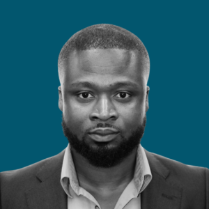 Portrait of a man with a serious expression, wearing a suit jacket and dress shirt, set against a teal background.