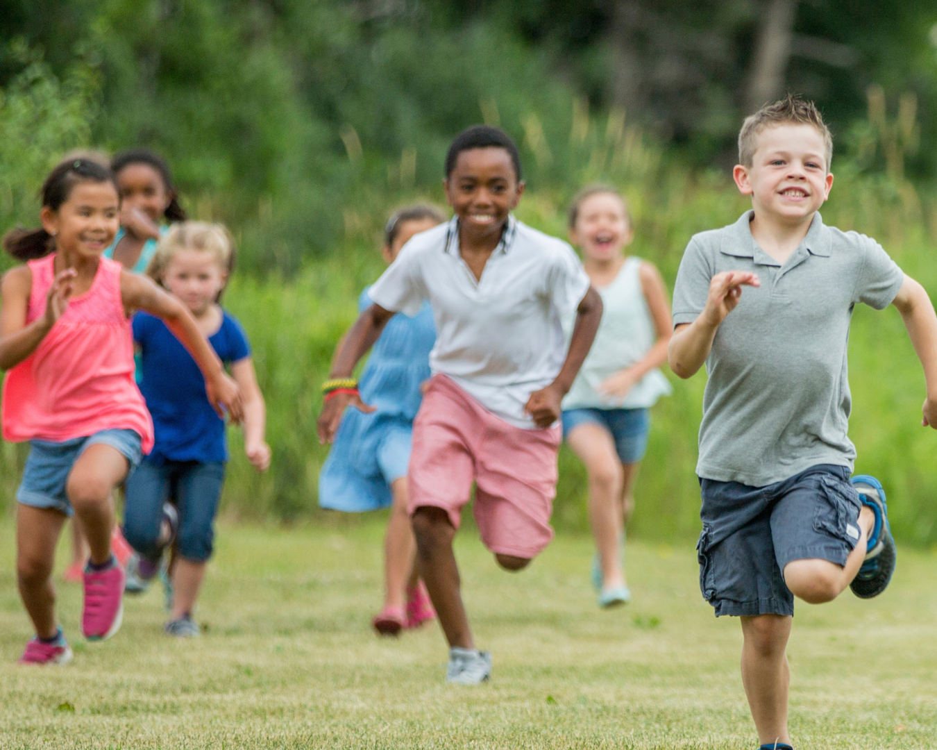 Children running outdoors in a grassy area with trees in the background.