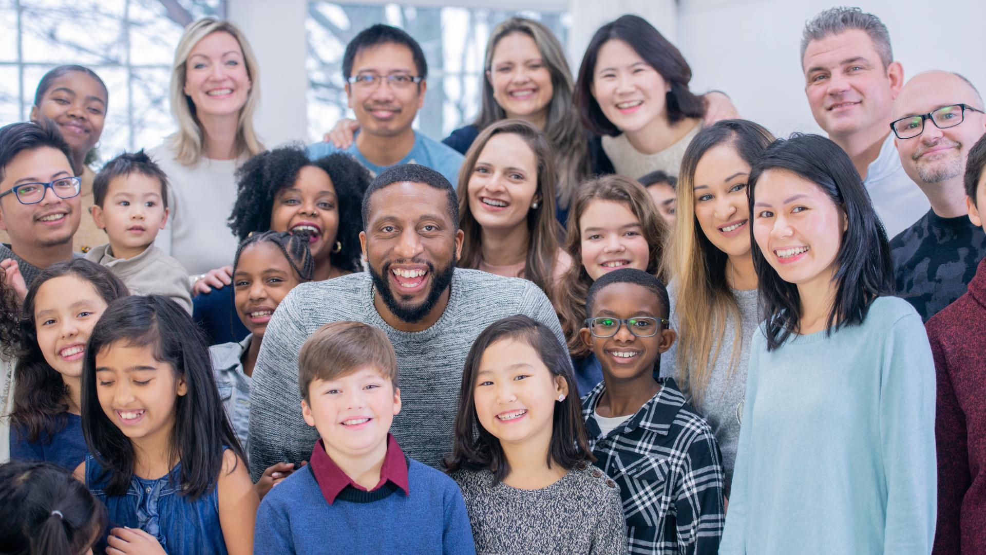 A diverse group of smiling people of various ages and ethnicities gathered together inside, facing the camera.