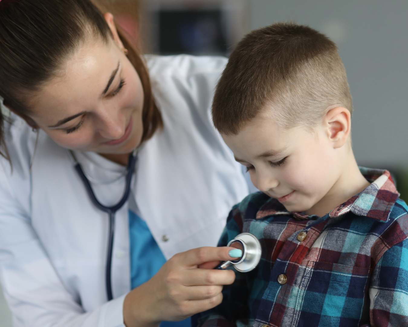 A female doctor or nurse using a stethoscope to listen to a young boy's chest in a medical setting.