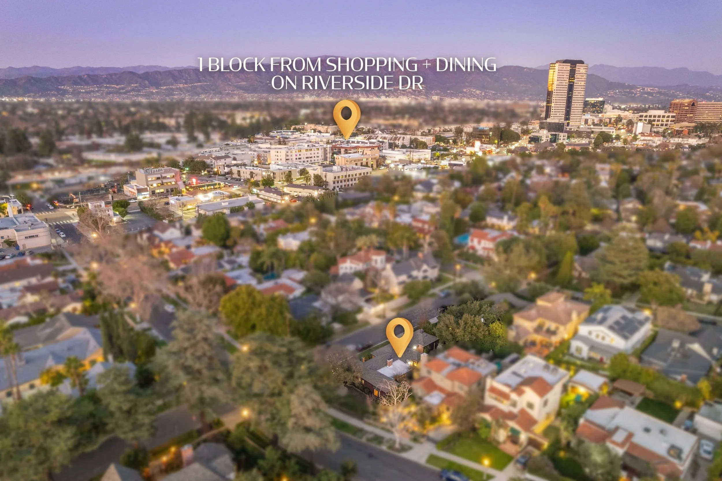 Aerial view of a cityscape at dusk, with residential houses, commercial buildings, and mountains in the background. Two location pins highlight specific areas, with one near the center and one toward the bottom of the image.