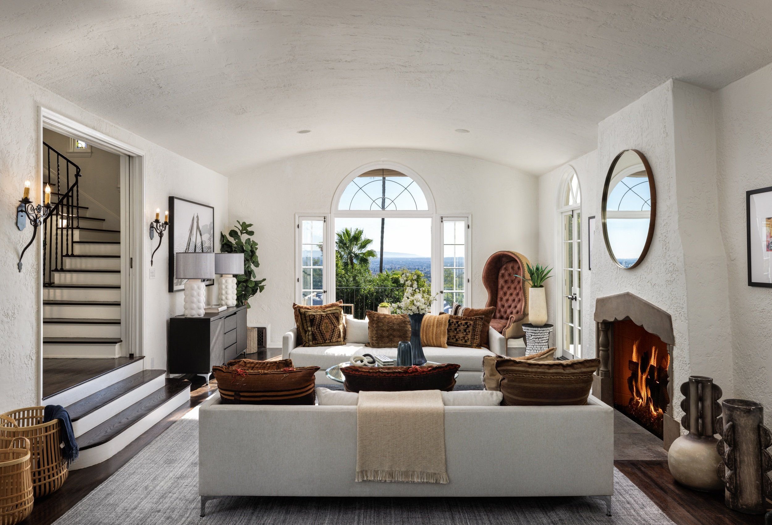 Living room with white sofa, patterned pillows, fireplace, and large window showing an outdoor view.